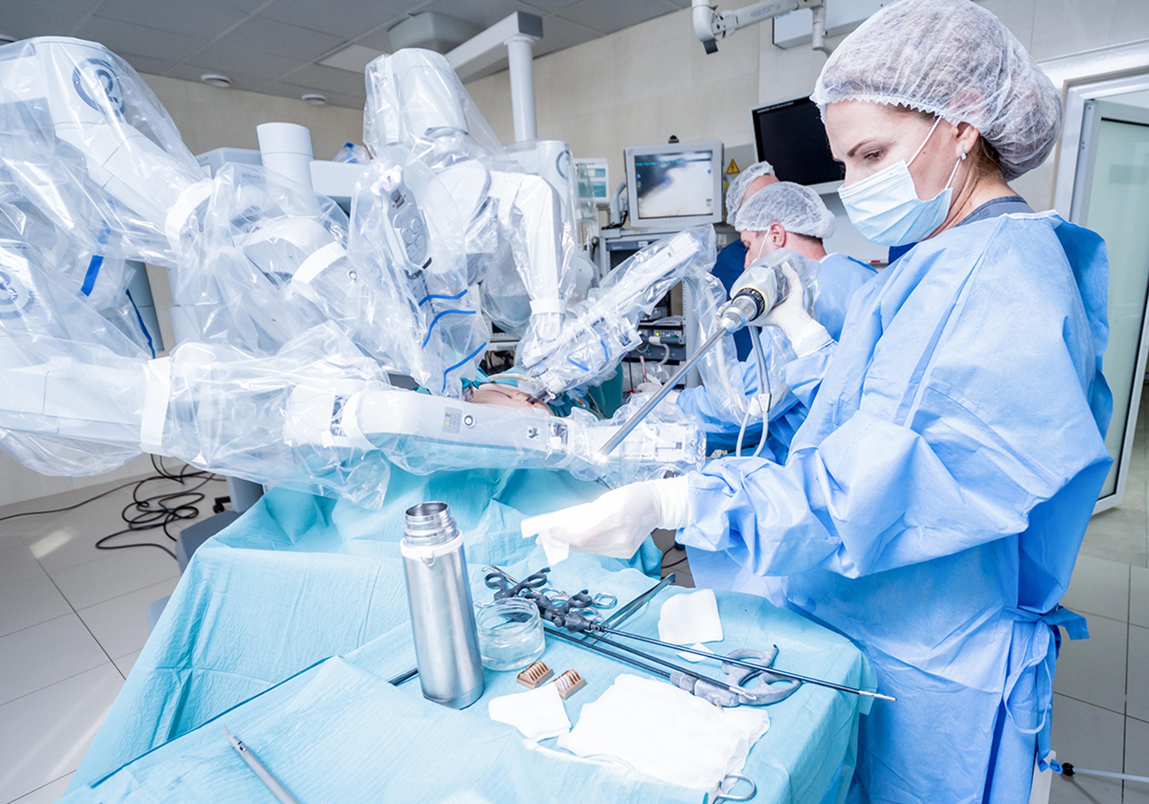 Surgeon in protective clothing operating a robotic-assisted surgical system in a hospital operating theatre during a minimally invasive procedure, illustrating advanced laser-enabled medical diagnostics and precision laser surgery technology.
