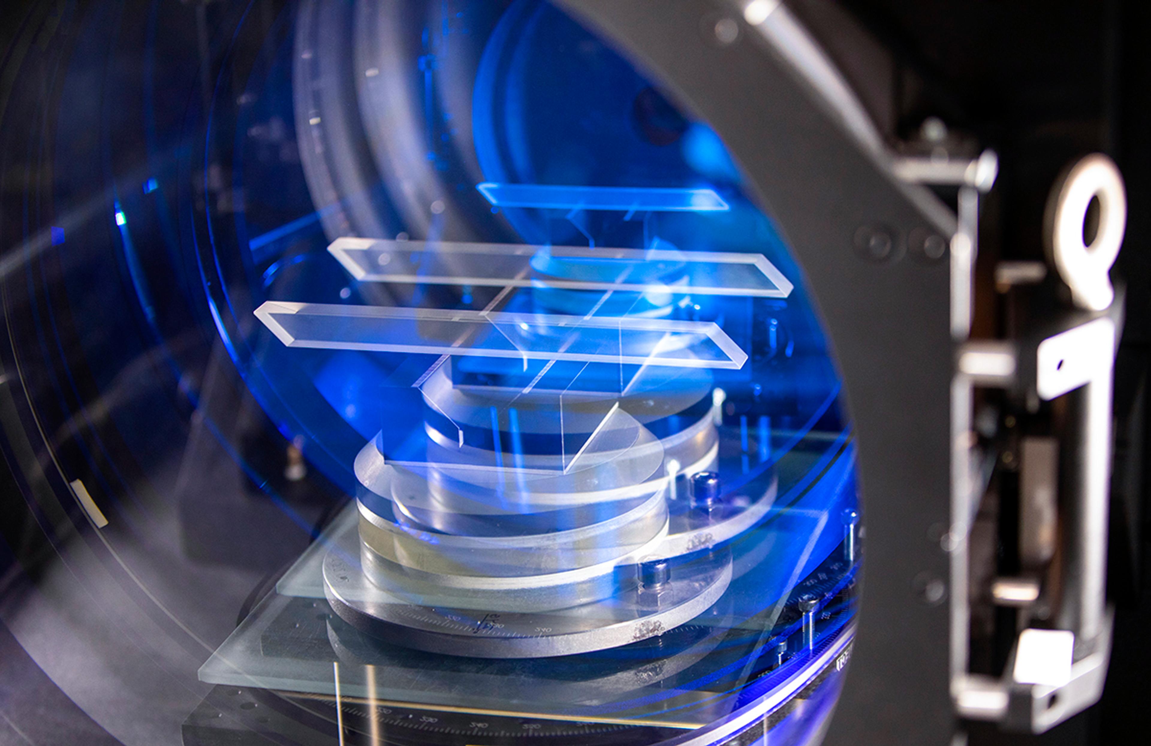 Close-up of precision optical components positioned inside advanced optical metrology equipment and illuminated with blue light during inspection and measurement.
