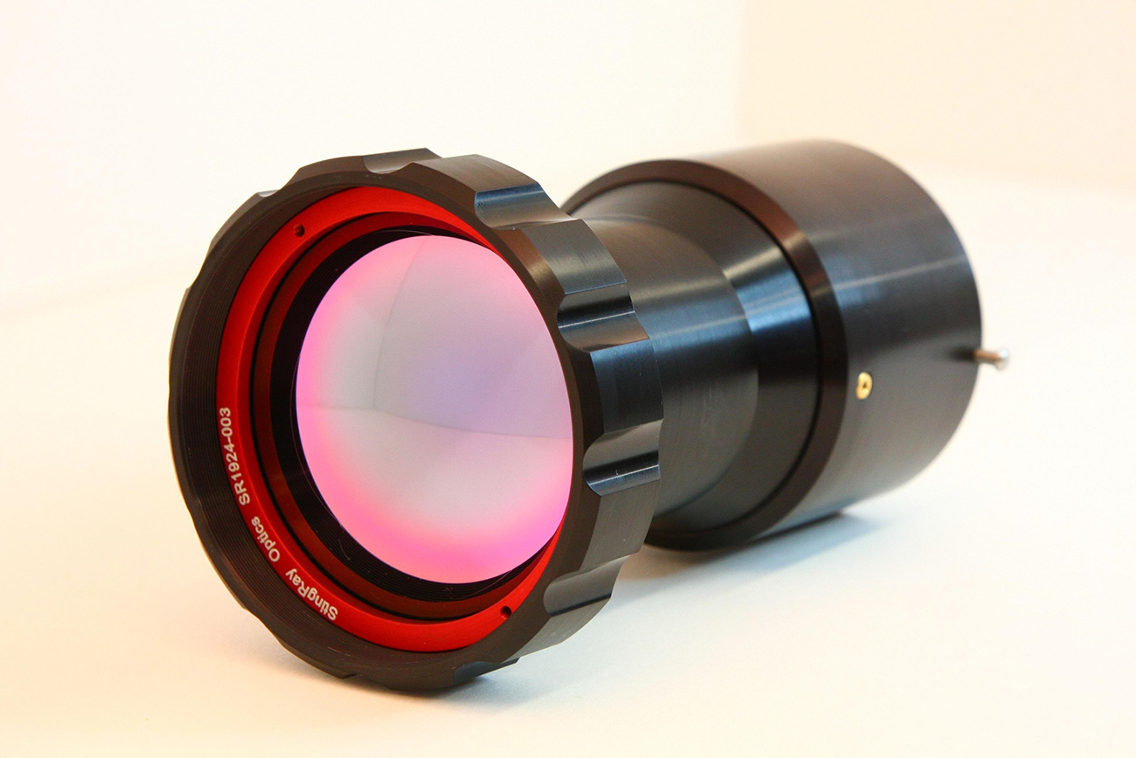 Close-up of a StingRay Optics Crimson 8–12 µm lens with a large aperture, red internal ring, and anti-reflective coated glass, placed on a light surface.