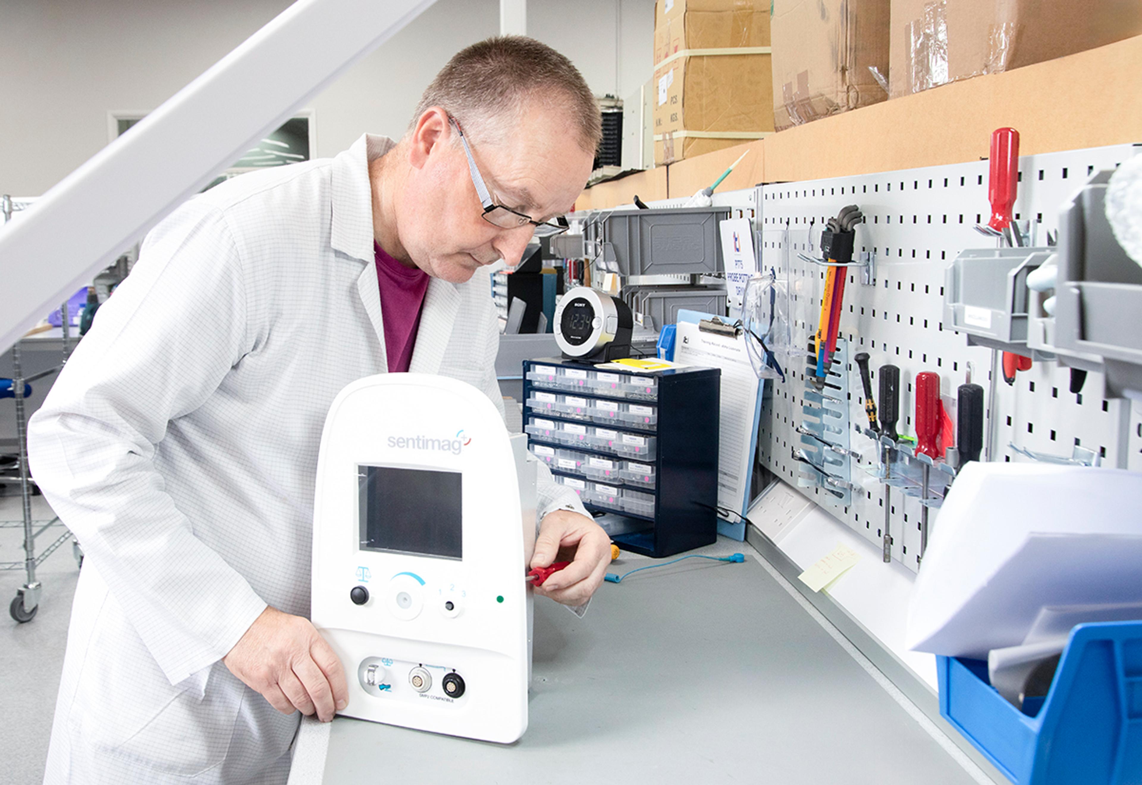 G&H | ITL technician assembling or testing a medical device at a workbench in a clean manufacturing environment.