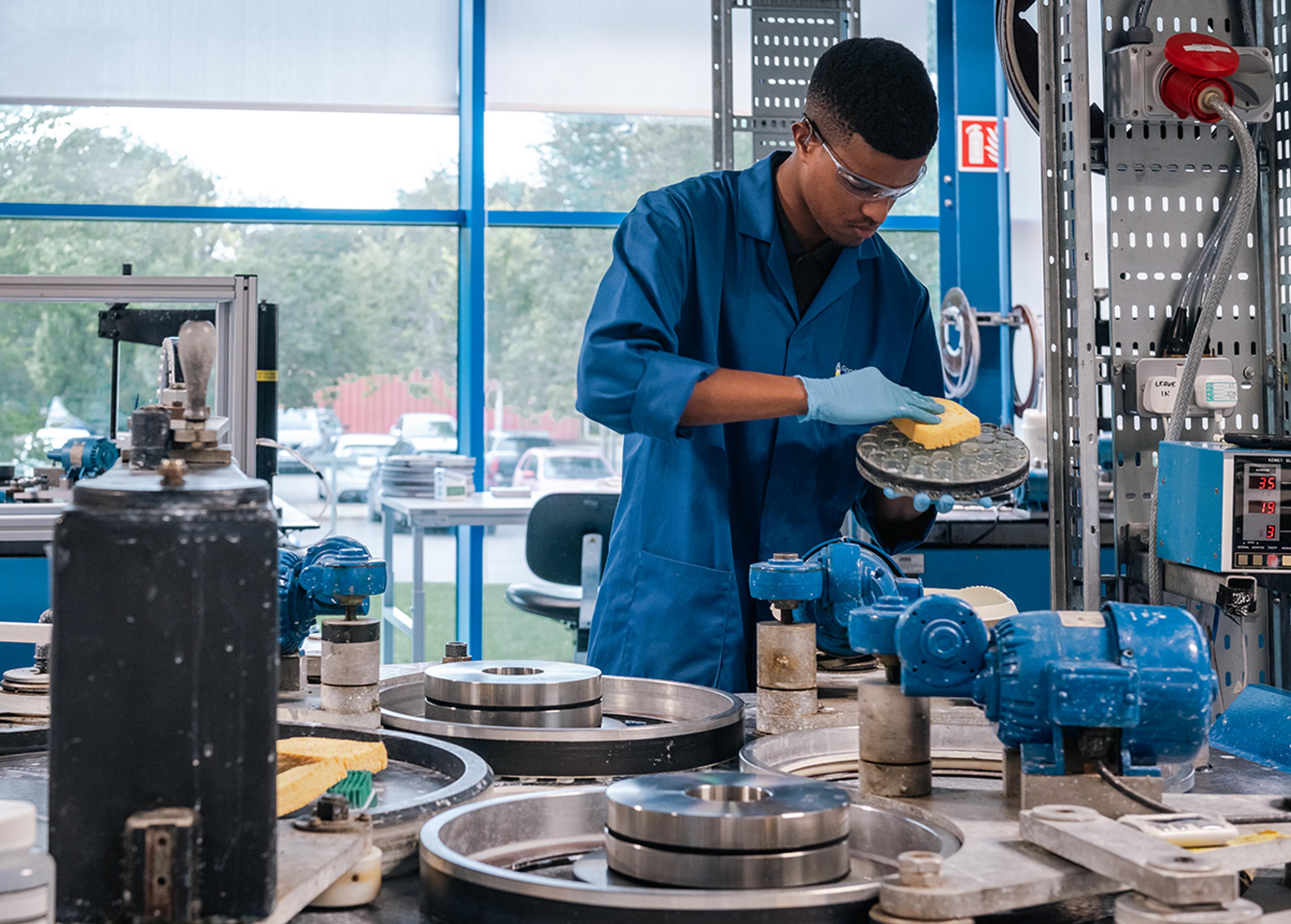 G&H technician carefully cleaning a polishing fixture containing multiple precision optical components in a specialist optics manufacturing facility.
