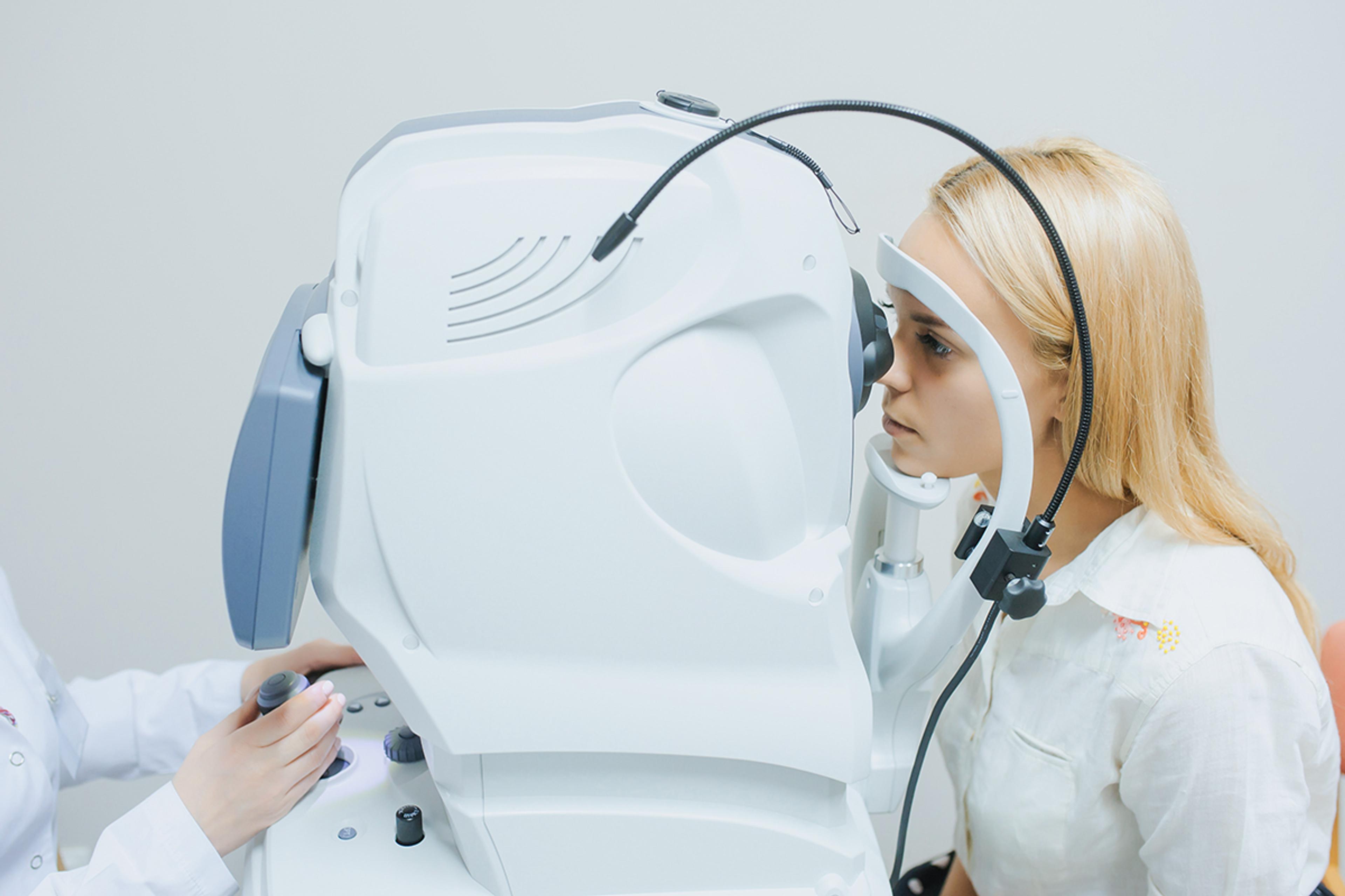 Patient undergoing an optical coherence tomography (OCT) eye examination using a laser-based ophthalmic imaging system, while a clinician operates the diagnostic equipment.
