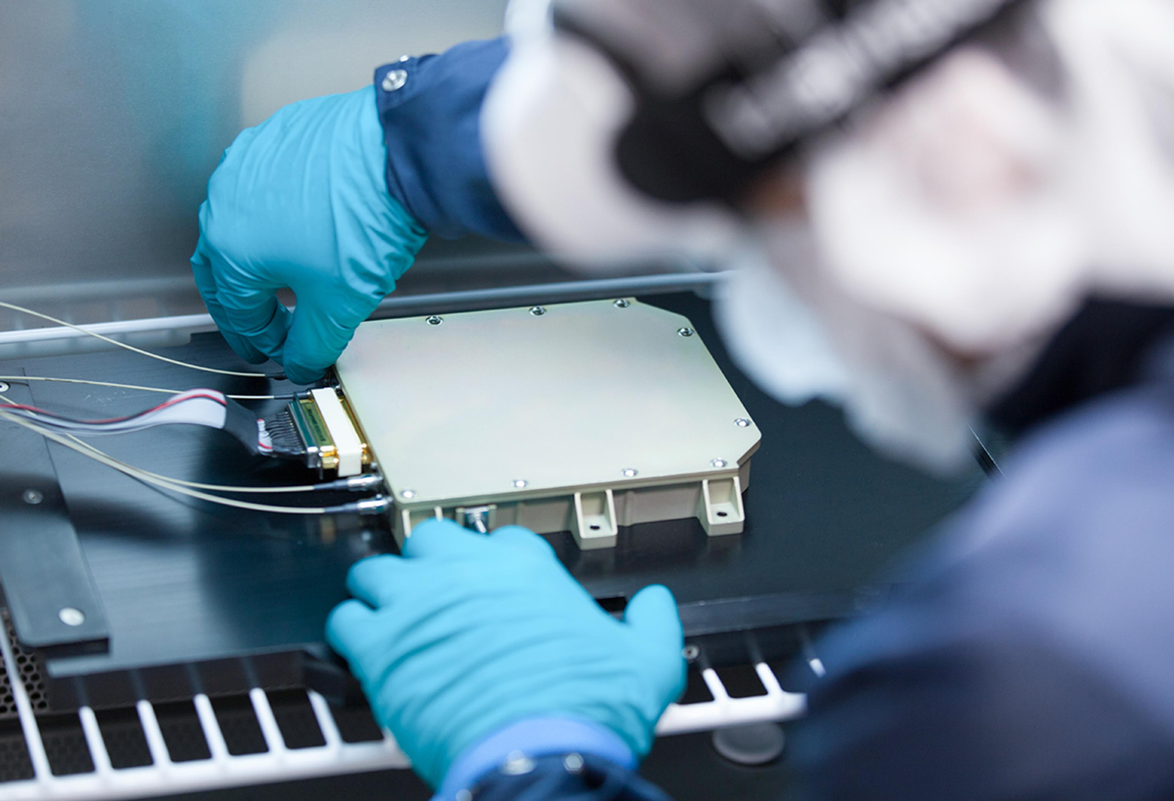 G&H technician wearing protective gloves assembles a high-performance fiber optic module, connecting fine optical fibers and electrical interfaces at the Torquay manufacturing facility.