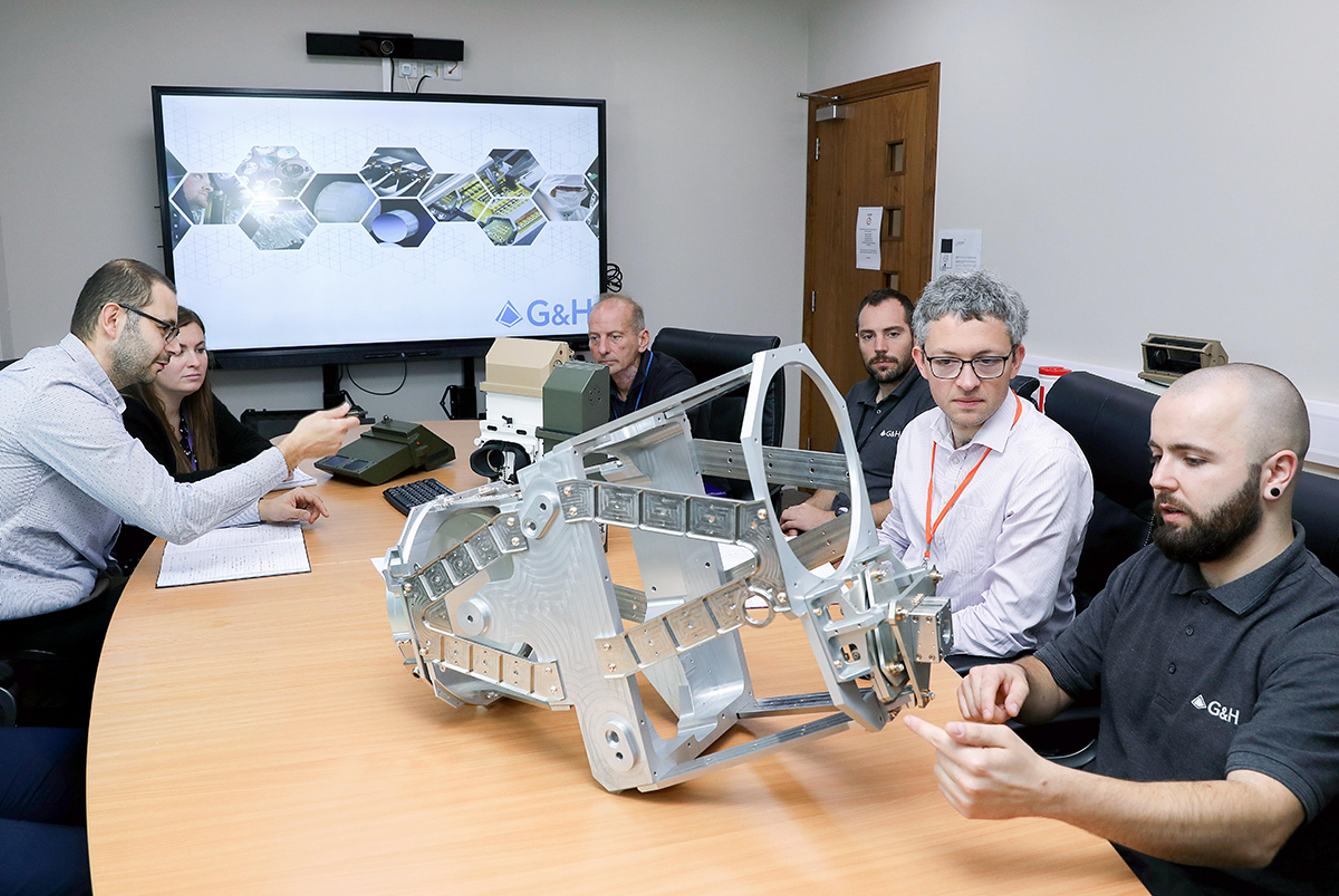 G&H engineering team reviewing a complex optical and mechanical system assembly and various periscope vision systems during a technical design meeting at the St Asaph Optical Systems Innovation Hub.