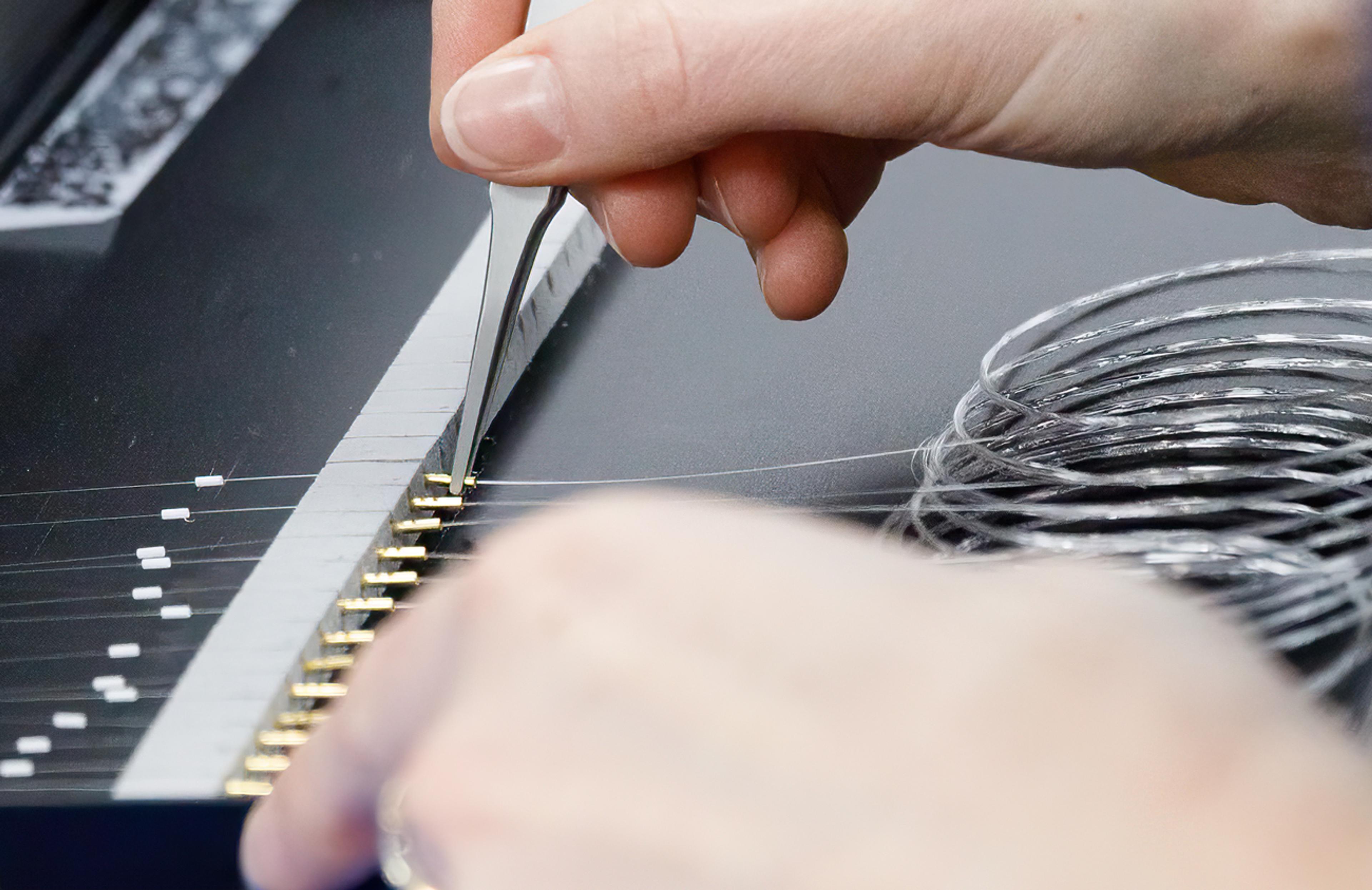 Close-up of a technician using tweezers to position fine fibre wires onto a row of gold contact pins during precision assembly.
