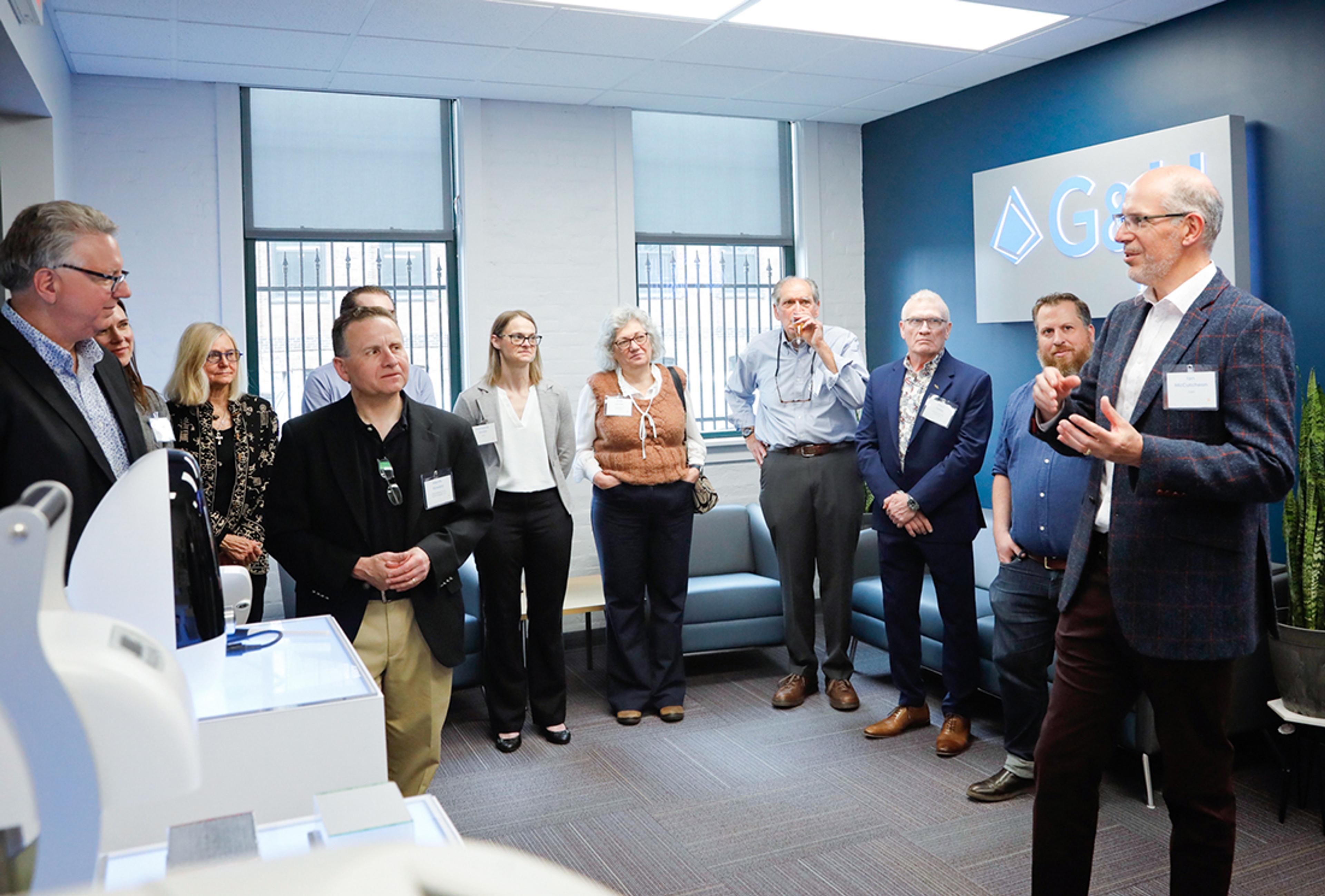 One of the G&H tours during Innovation Hub grand opening. Many people in a room with G&H logo on the wall and life sciences products on display