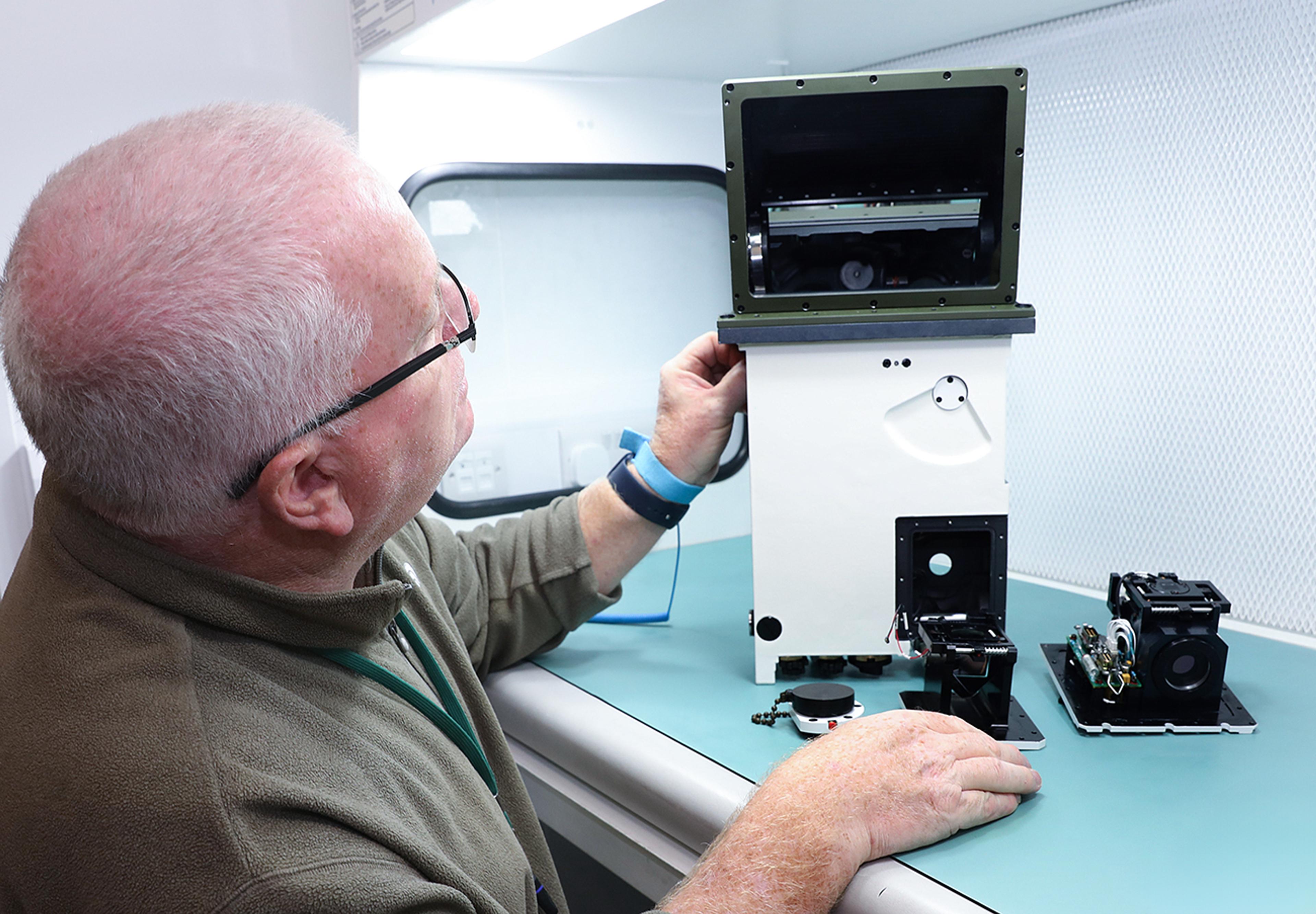 G&H engineer inspecting a precision periscope sighting system and associated optical components during assembly and testing.