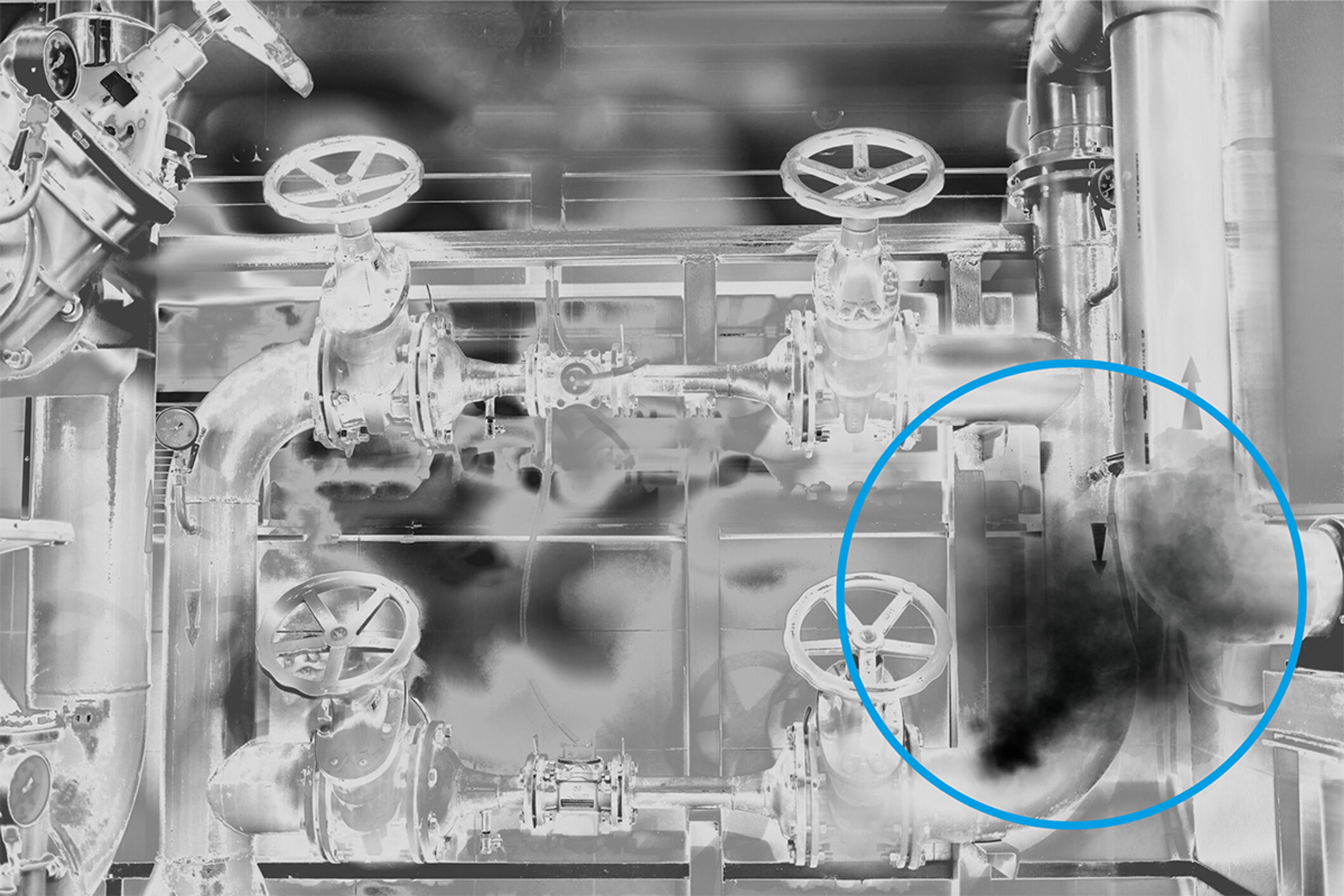 Optical Gas Detection (OGI), A high-contrast, grayscale image of an industrial pipeline system with multiple valves and gauges. A thick dark plume, indicating a gas leak, is visible in the lower-right quadrant and highlighted by a bold blue circle. The image demonstrates optical gas detection technology used to visualize gas leaks that are invisible to the naked eye.