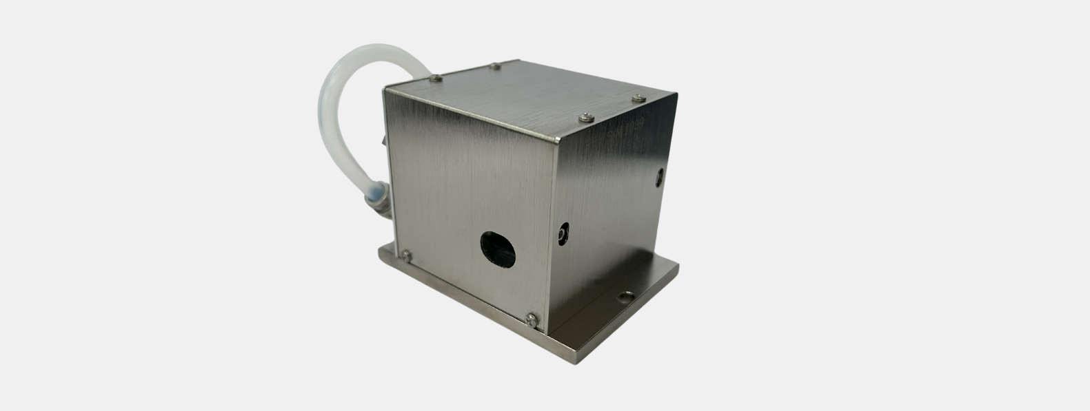 AODF-UV A compact, stainless steel industrial device with a rectangular metal housing mounted on a flat base. The front face has a circular black opening and a small port or screw hole. A translucent flexible tube is attached at the back, curving upward and to the side. The unit is secured with multiple small screws on the top and sides, and the brushed metal finish gives it a clean, durable appearance. The background is plain white, emphasizing the device's design
