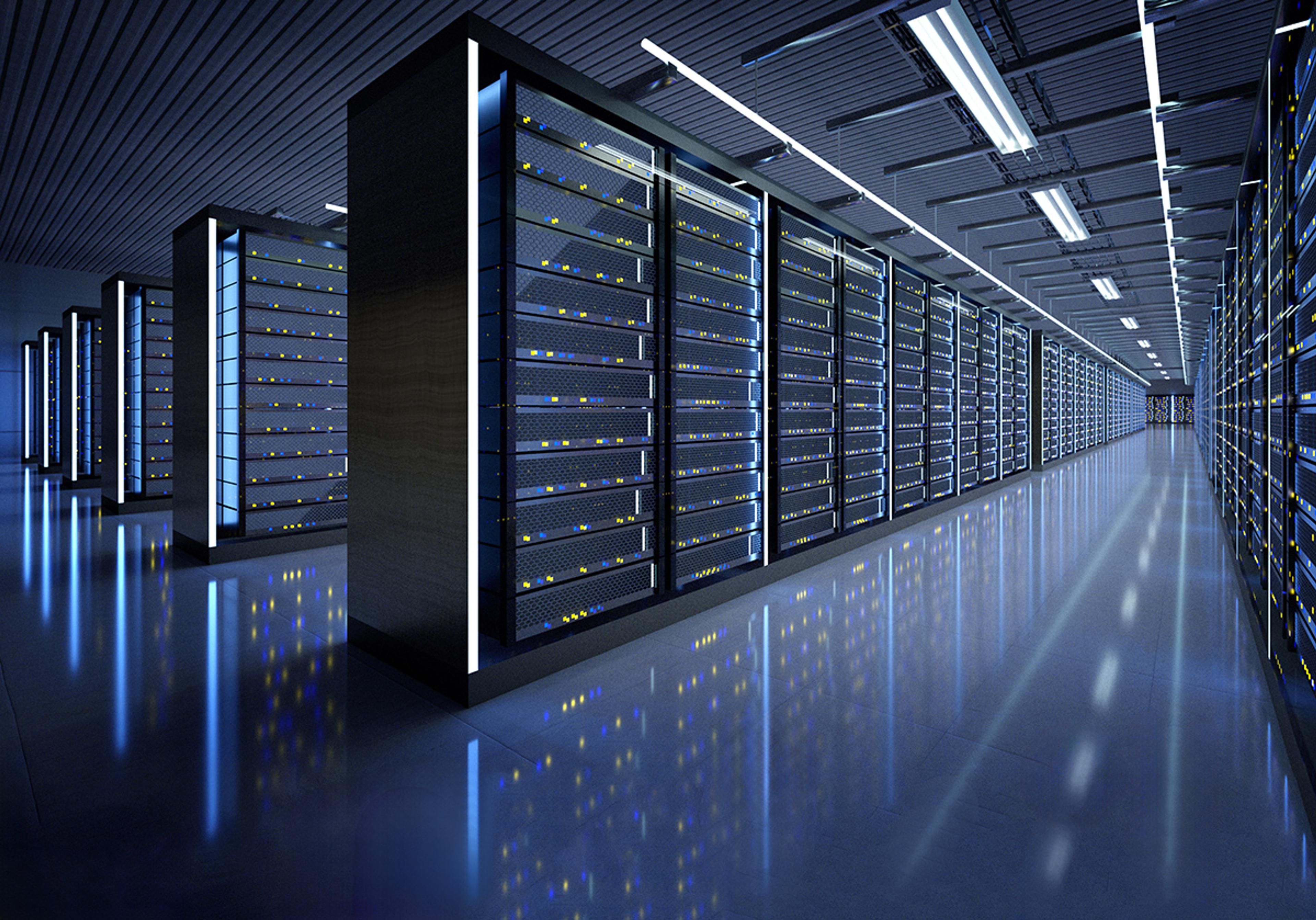 Wide view of a modern data centre with long rows of illuminated server racks and reflective flooring under bright overhead lighting.