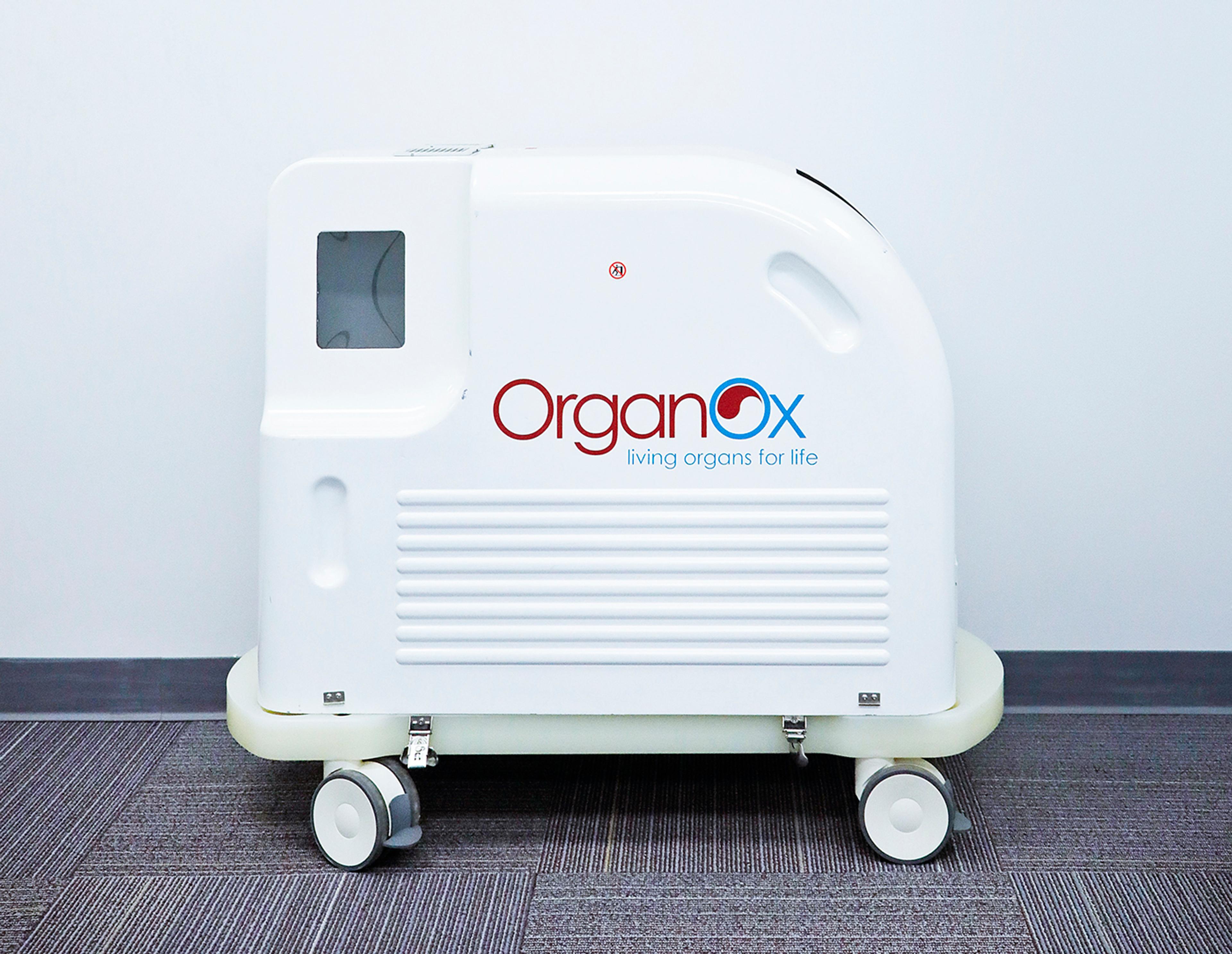 White OrganOx medical device on wheels with the logo “OrganOx – living organs for life,” photographed against a plain indoor wall.