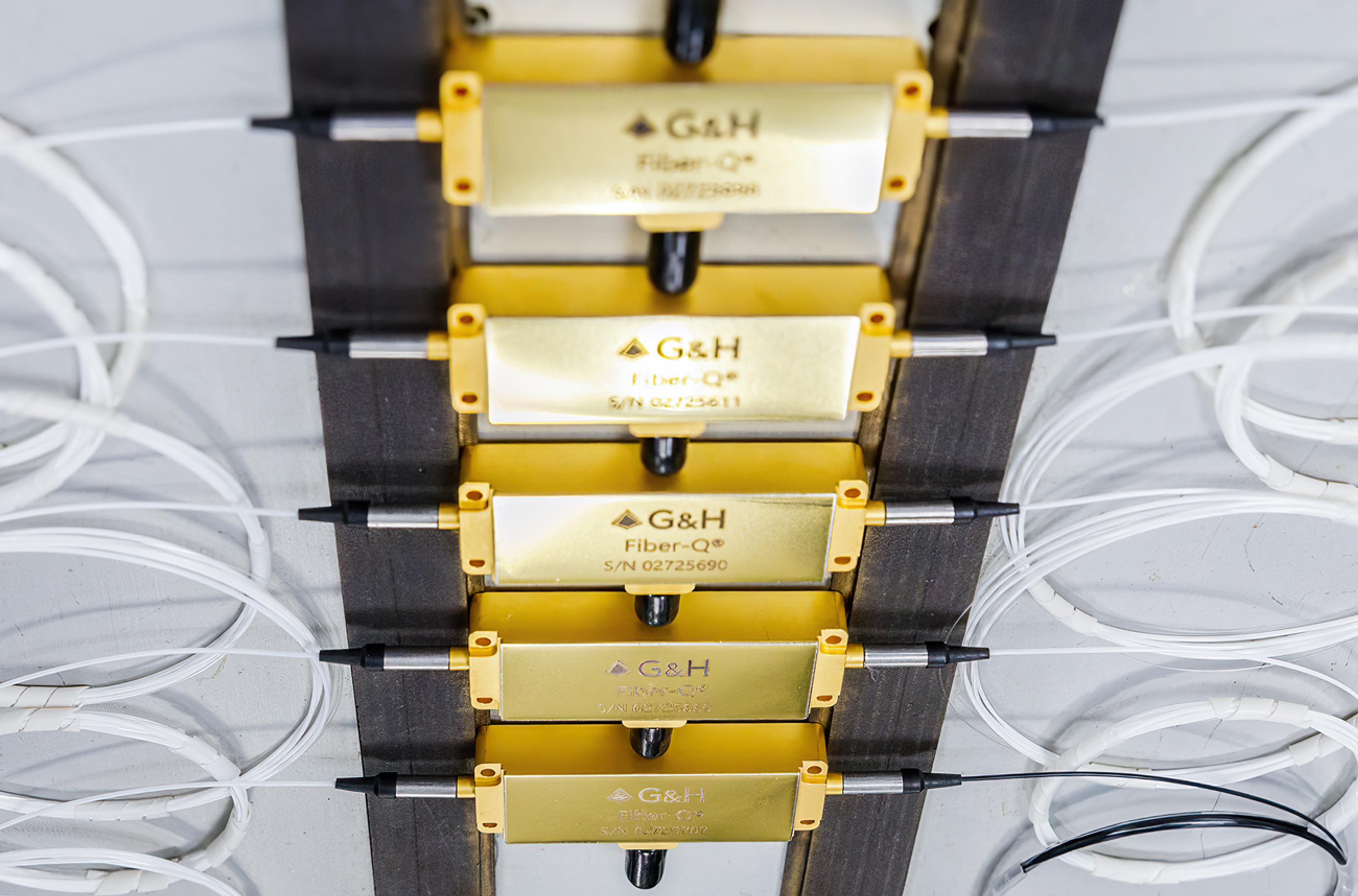 Tray of gold fibre-optic modules with connectorised leads and coiled white fibres arranged for inspection or testing.
