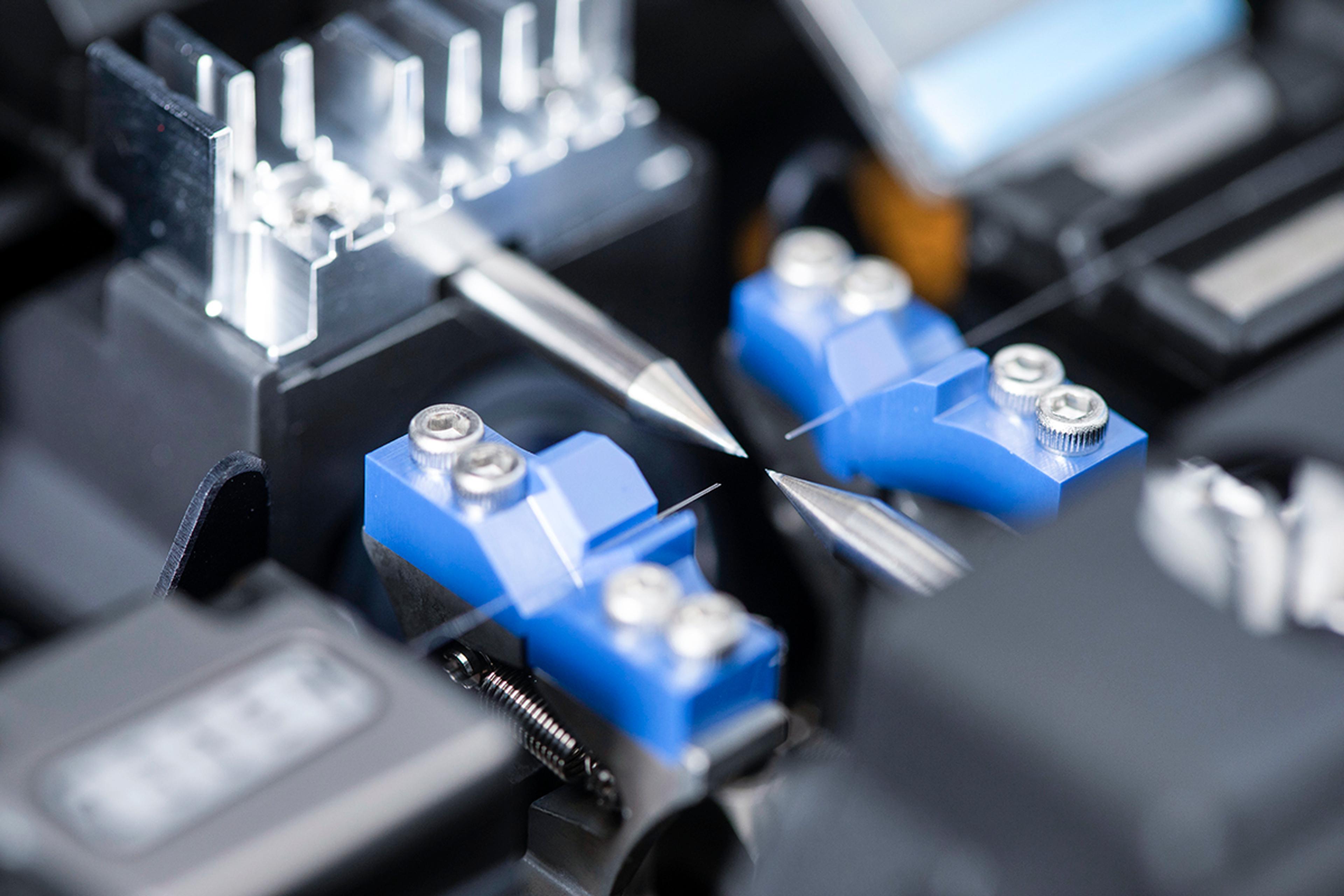 Close-up of a precision fiber optic component held in a quality assurance test fixture with alignment clamps and measurement probes at G&H Torquay.