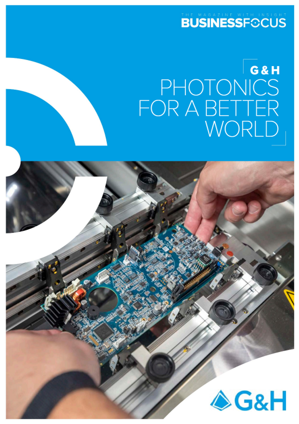 Front cover of Business Focus magazine featuring G&H with the headline “Photonics for a Better World.” The design includes a vibrant blue header with the G&H logo, and a large image showing hands placing a circuit board into a manufacturing fixture—highlighting precision photonics and electronic assembly. G&H branding appears prominently at the bottom.