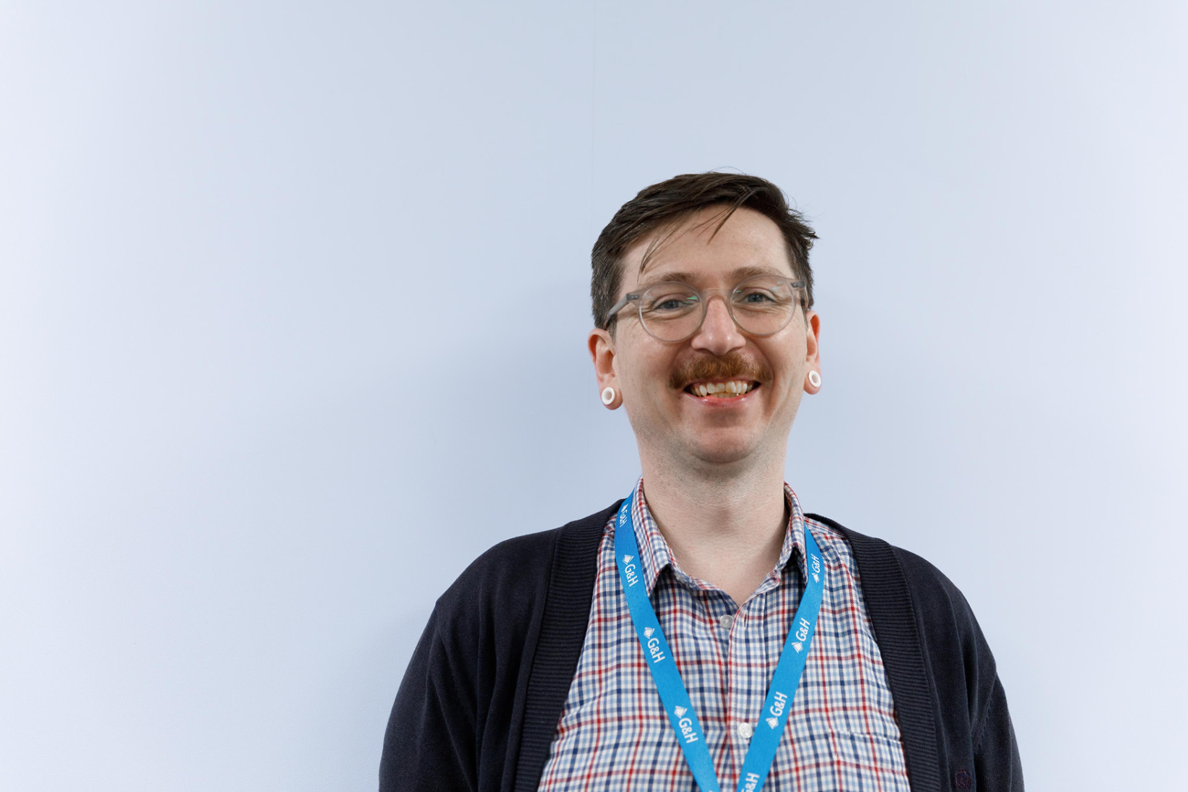Smiling G&H employee wearing glasses and a company lanyard, standing against a neutral background in an office or workplace setting.