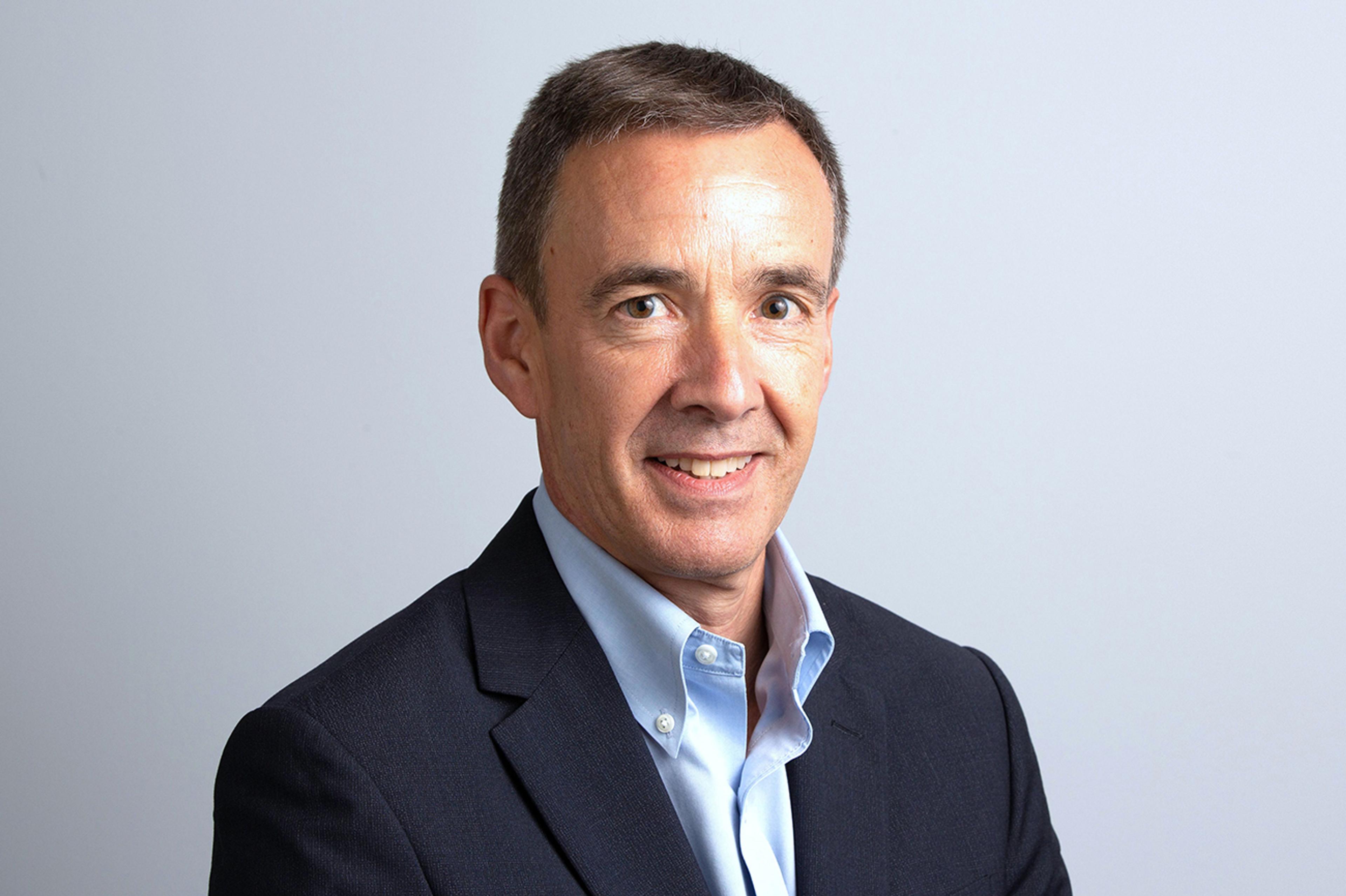 Chris Jewell – Chief Financial Officer - Portrait of a middle-aged man in a dark navy blazer and light blue shirt, smiling at the camera. He has short dark hair with some gray, and the background is a plain light gray color.