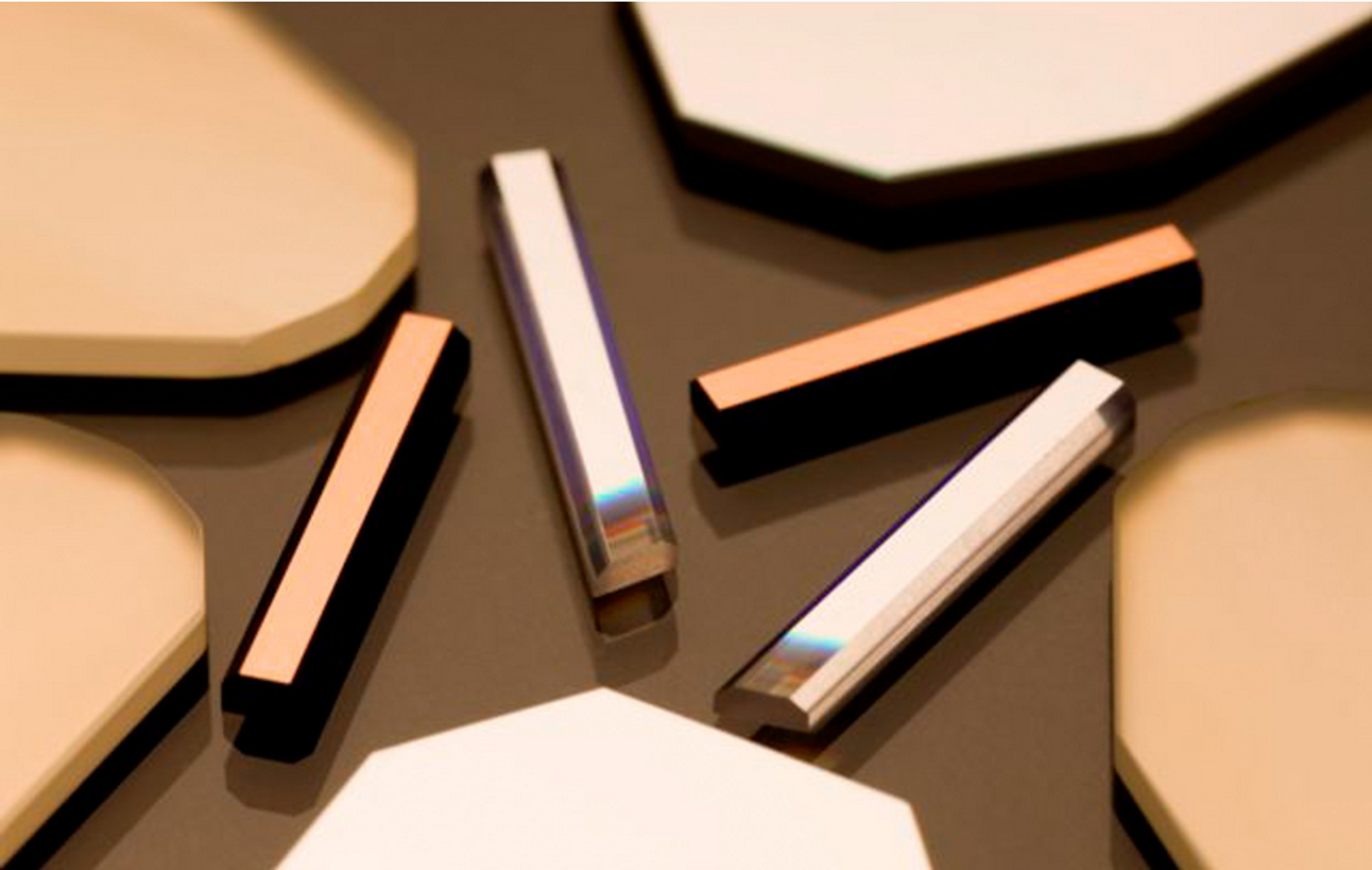 A collection of rectangular and octagonal optical filters and mirrors displayed on a reflective surface. The rectangular filters vary in coating—some appear metallic or copper-toned, while others are highly polished and coated with iridescent layers, reflecting spectral hues. The octagonal components are uniformly pale with a matte finish, suggesting precision-engineered optics.