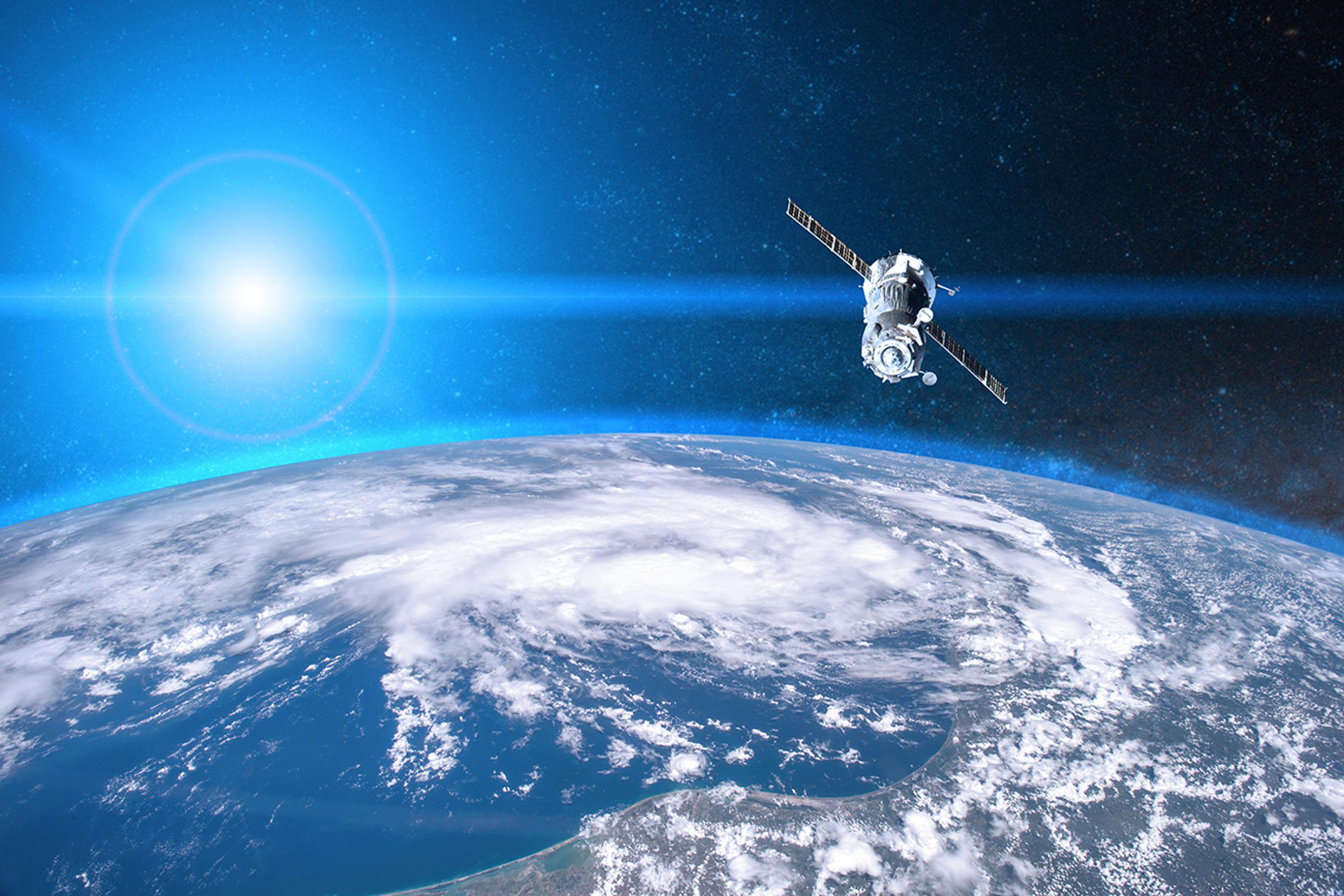 Satellite orbiting above Earth with the sun glowing in the background and a visible weather system over the ocean, depicting space-based observation and communication technology