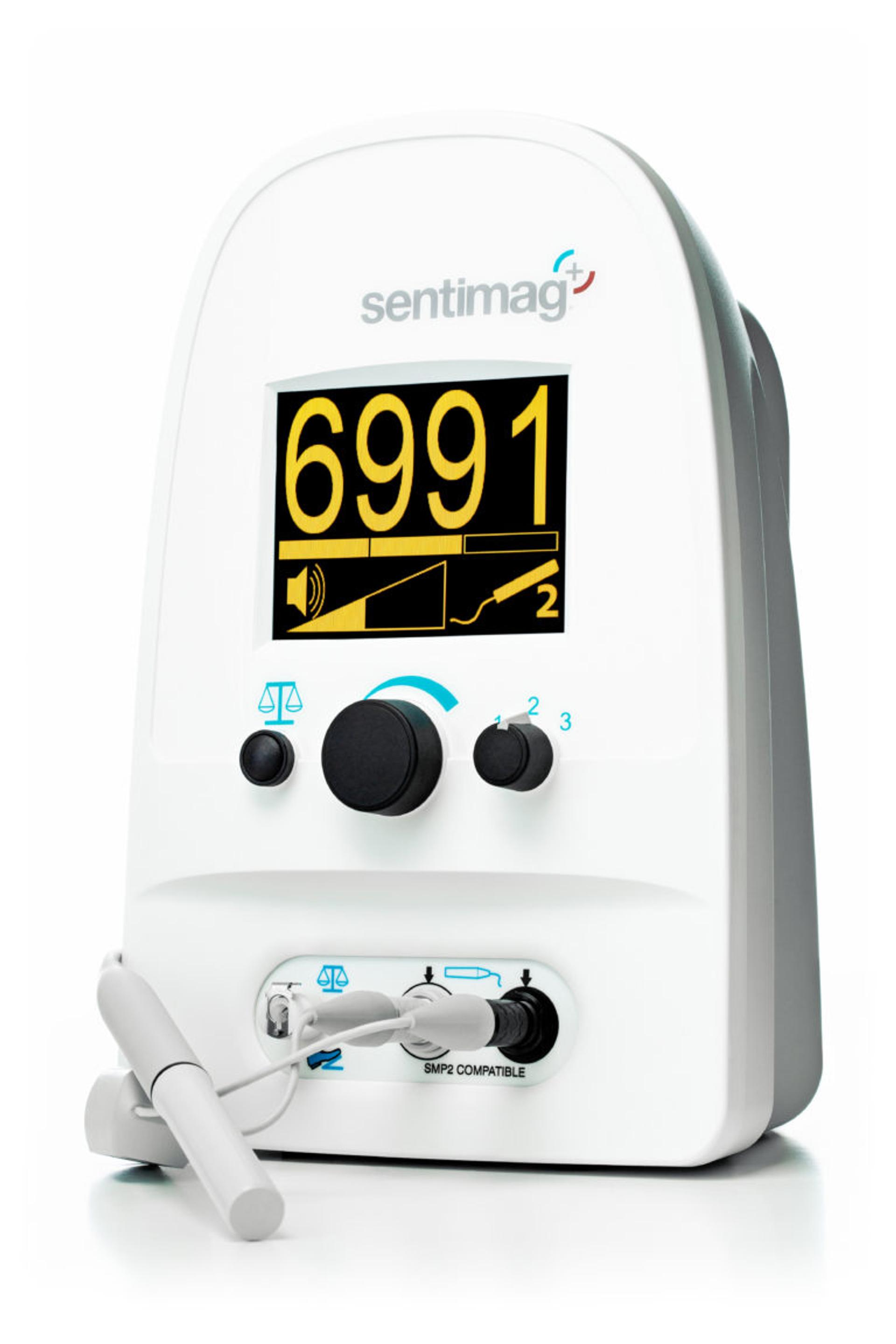 A close-up image of the Sentimag® device, a medical magnetometer used for detecting magnetic tracers during procedures. The device has a white casing with a prominent digital display showing the number "6991" in yellow, along with visual indicators for signal strength and volume. Below the screen are control knobs and ports labeled for compatibility. A connected probe is resting on the surface in front of the device.