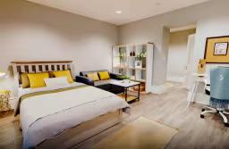 Bright studio apartment with a double bed, sofa, study desk, storage shelves, and an open-plan layout with contemporary furnishings.