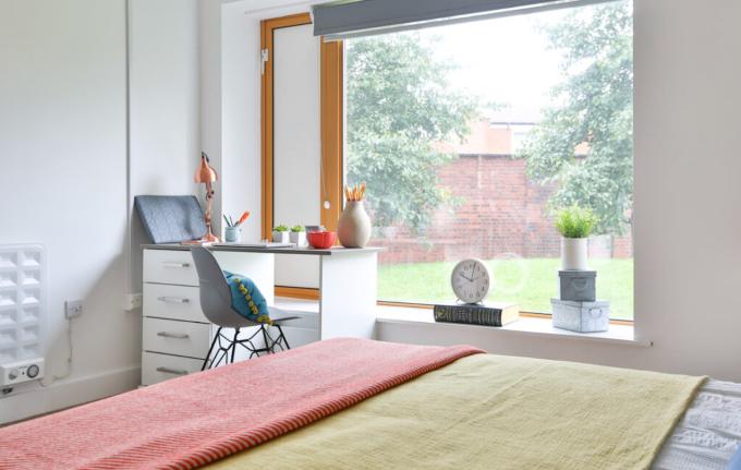 Bright student bedroom with a study desk, large window, chest of drawers, and a comfortable bed in a modern layout.