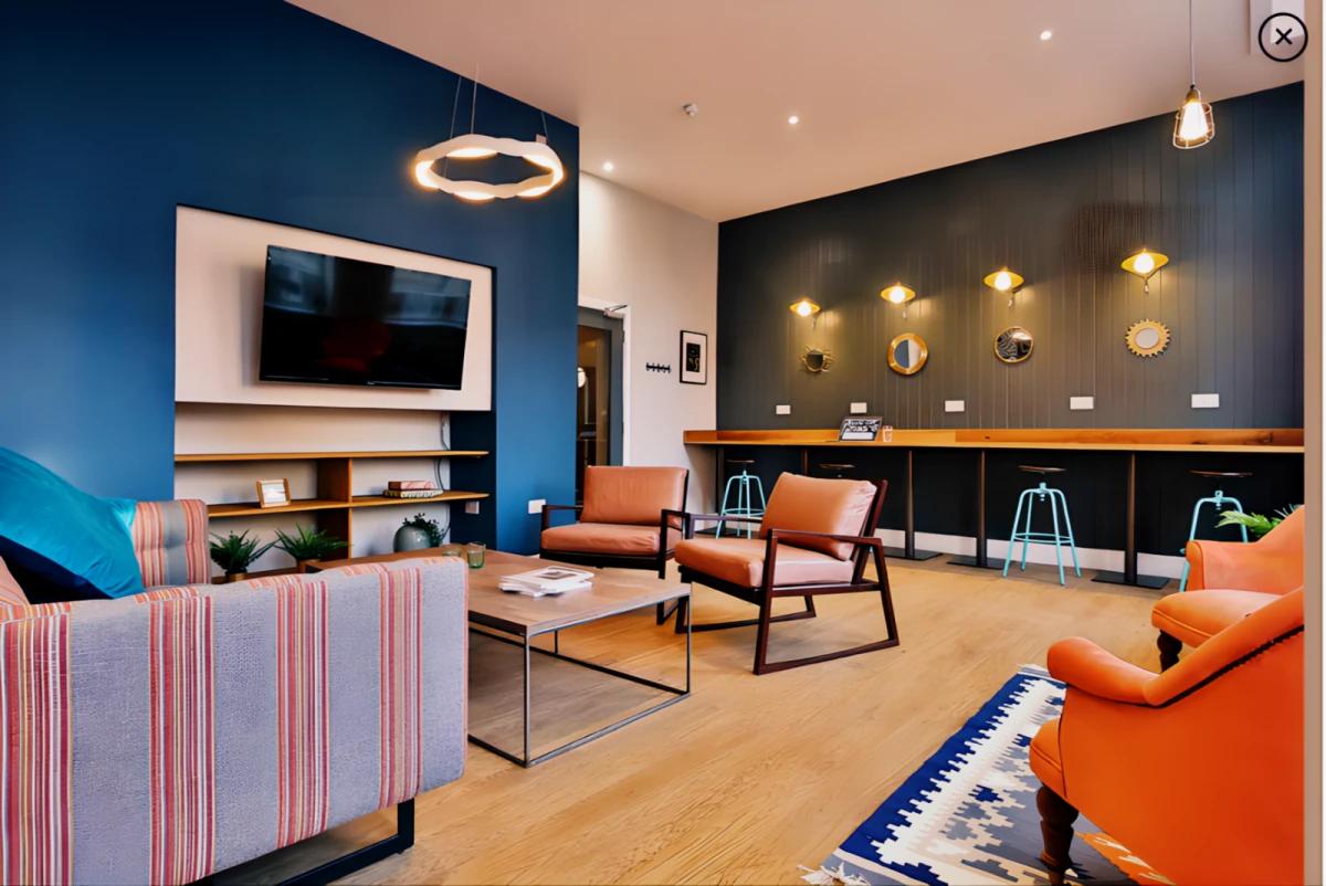 Stylish communal lounge with comfortable seating, wall-mounted TV, study bar, and modern lighting.
