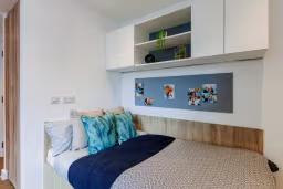 Student bed nook with patterned pillows and navy bedding, built-in white overhead cabinets, and a mounted pinboard with photos above the headboard.