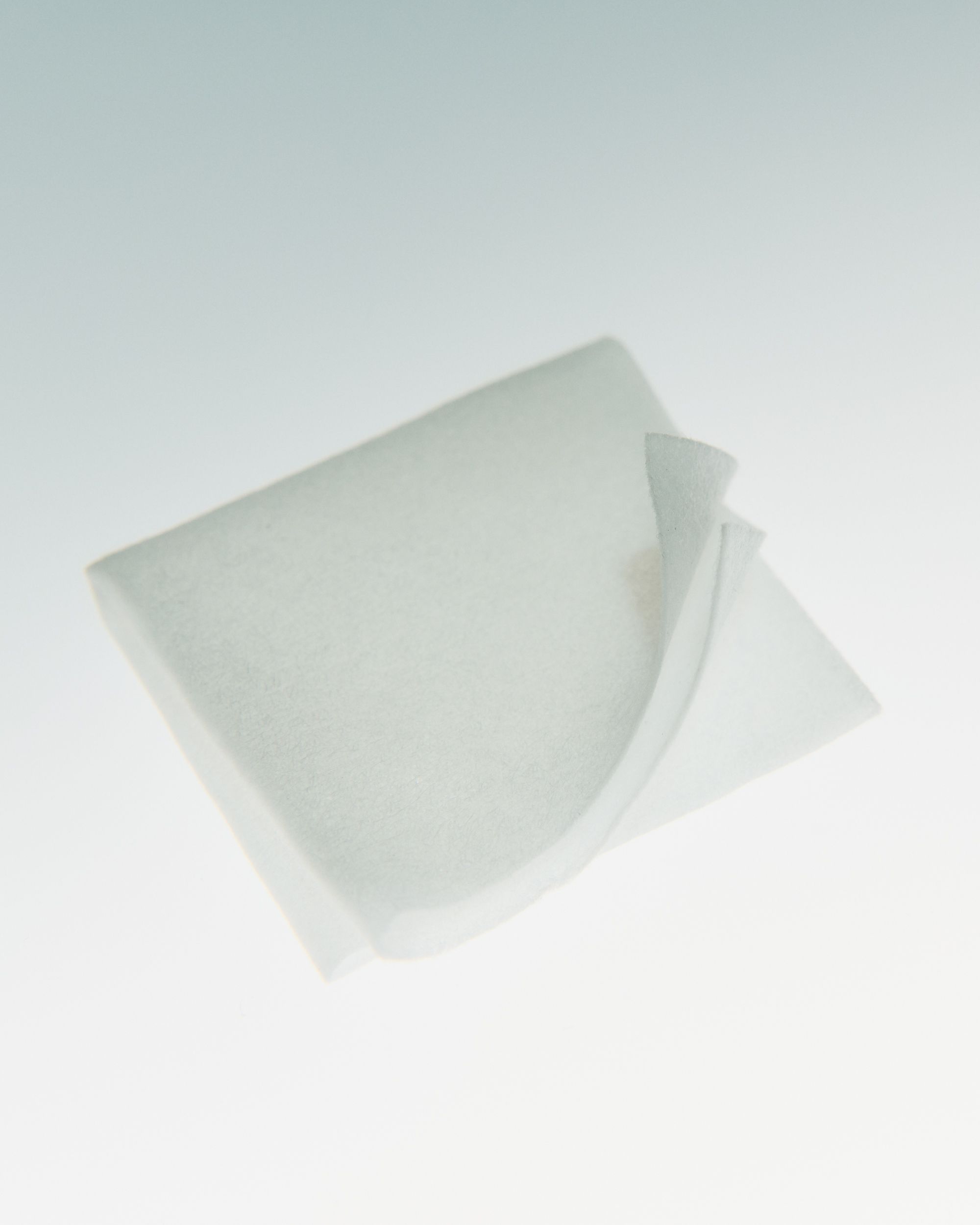 A white, translucent square sheet with one corner gently curled upward.
