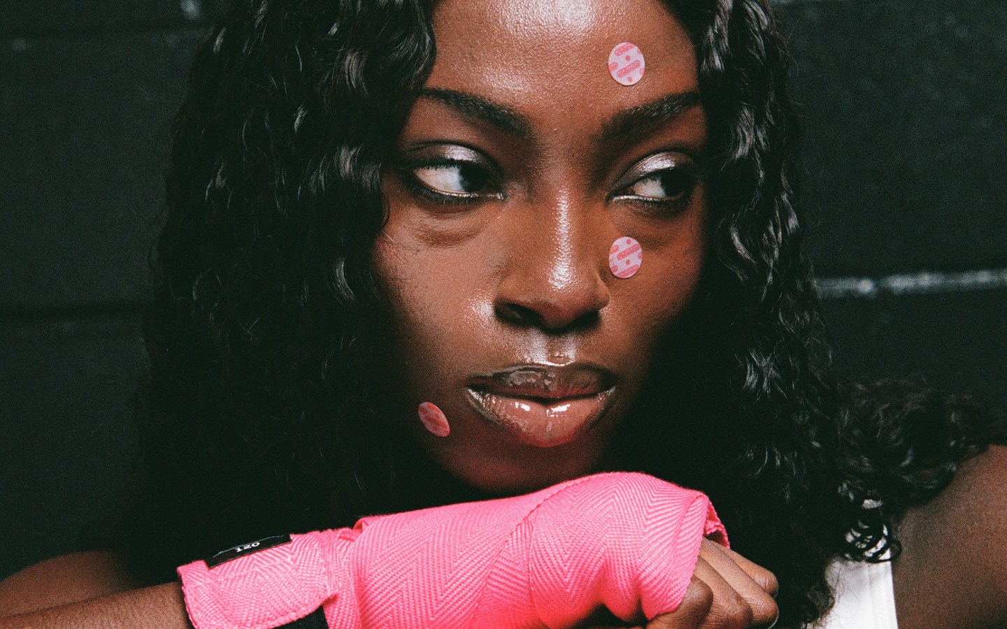 A young Black woman with pink acne patches on her face and a pink boxing hand wrap.