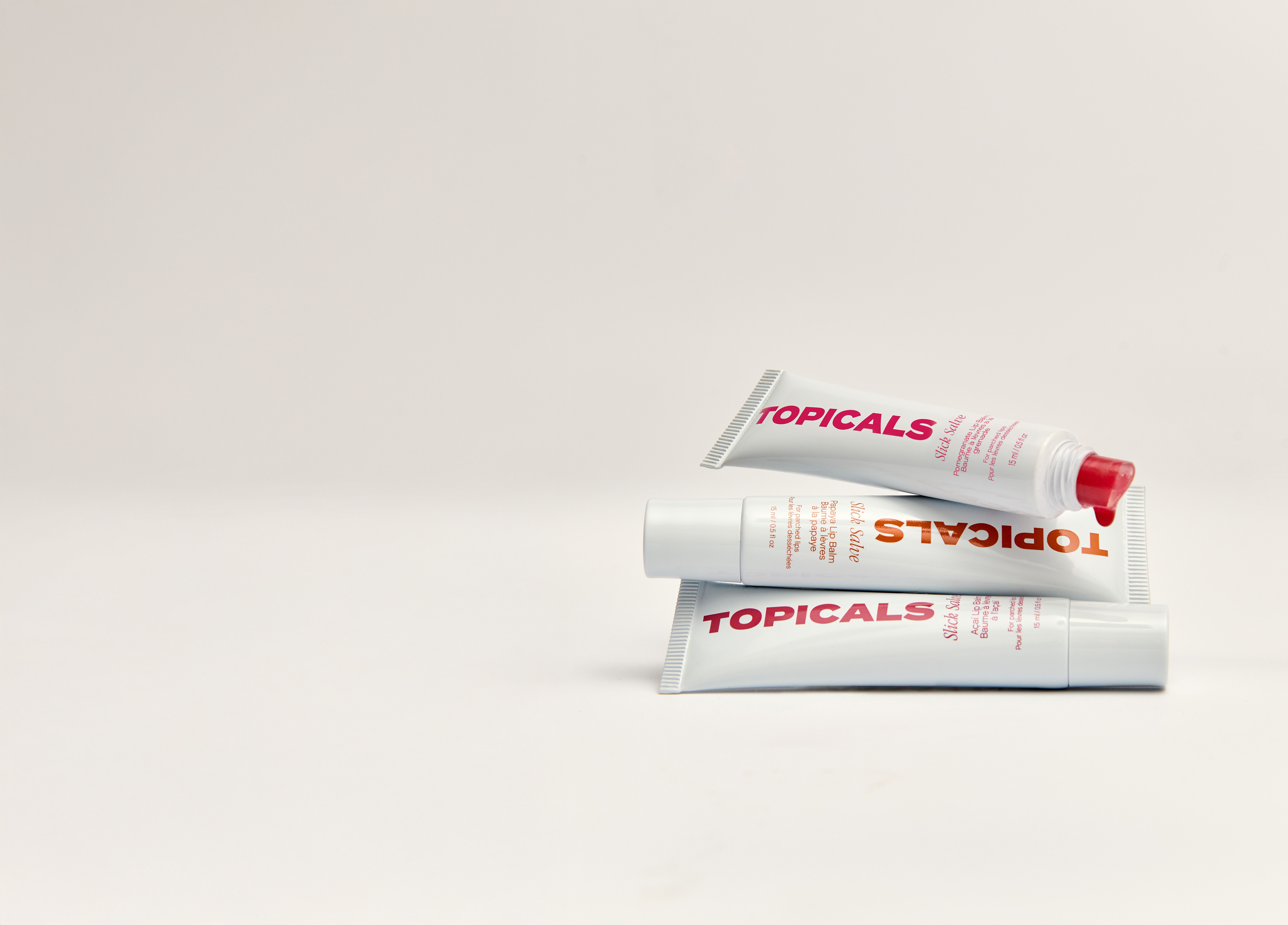 Three white tubes of TOPICALS cream, stacked, with the top tube showing a red cap and some red product.