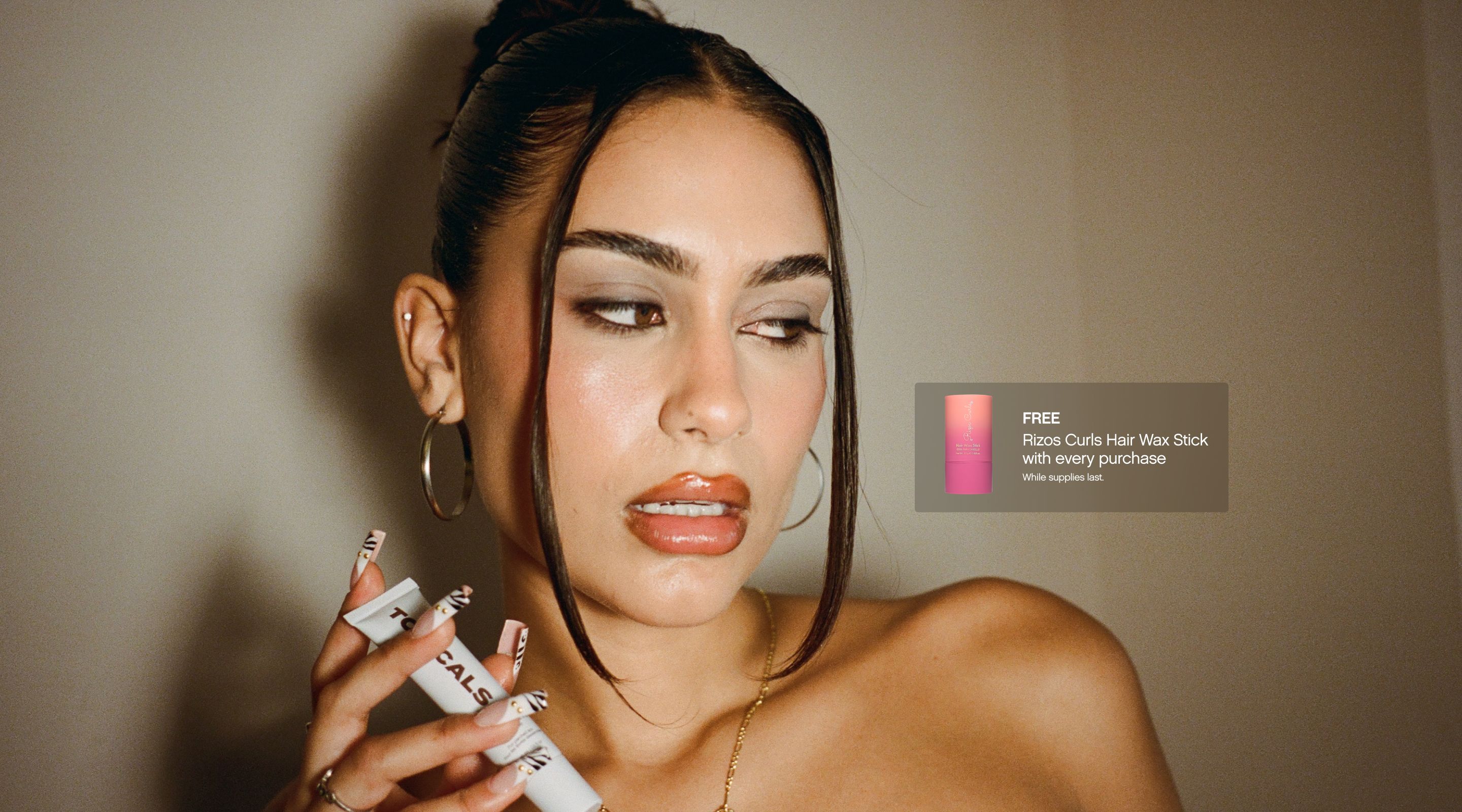 A woman with glossy lips and dark hair holds a white "TOPICALS" product; a text box to the right offers a "FREE Roze Curls Hair Wax Stick with every purchase."