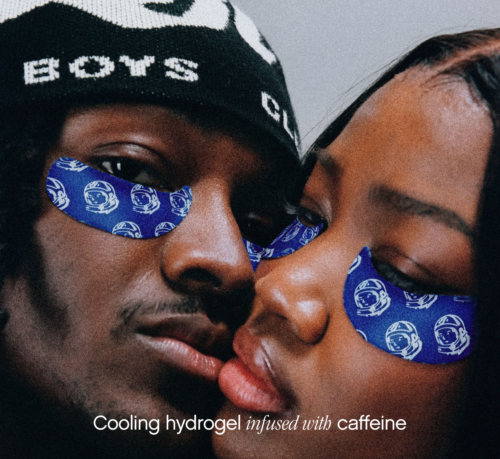 A man in a "BOYS CLUB" beanie and a woman wear blue under-eye patches with white astronaut helmets, close together. Text: Cooling hydrogel infused with caffeine.
