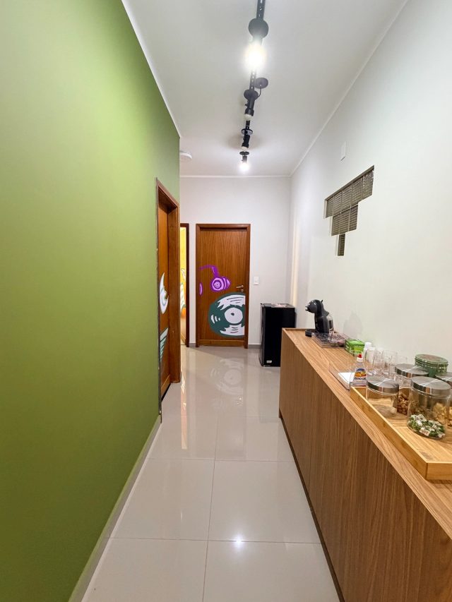 Corredor da agência com parede verde, portas grafitadas e a copa com cafeteira ao lado