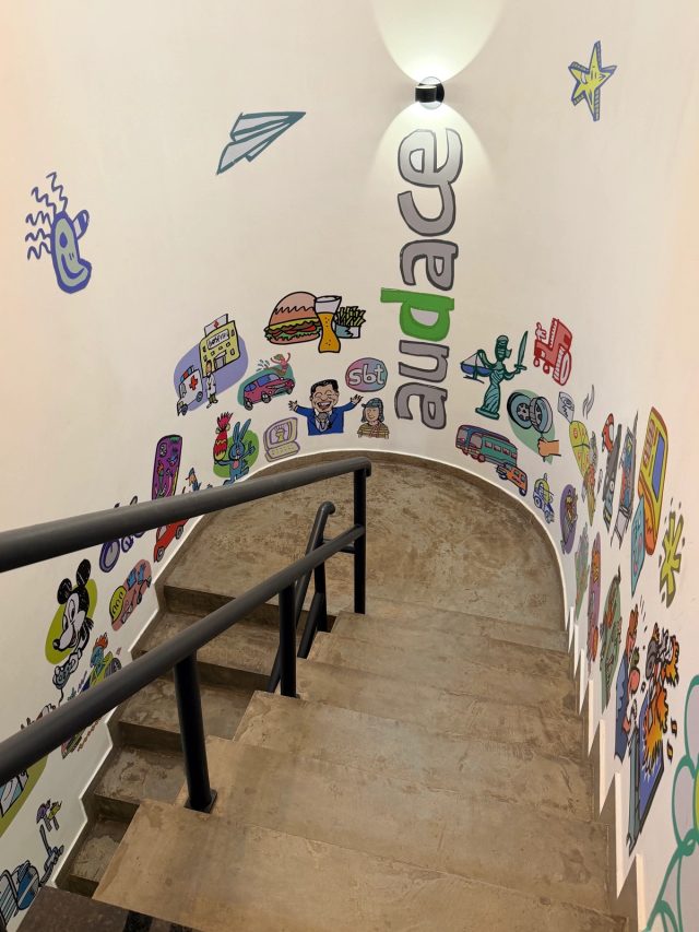 Escada da agência com mural colorido de ilustrações e o logo da Audace pintado na parede