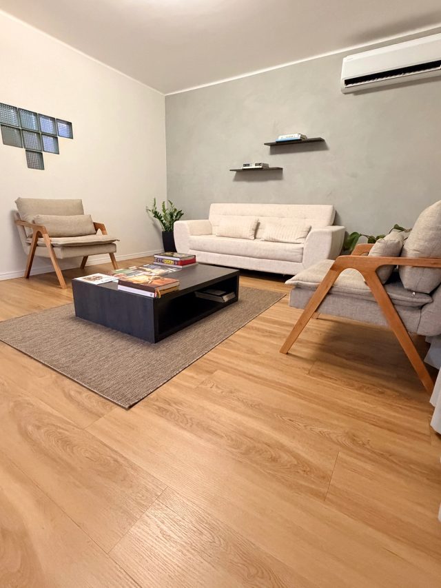 Lounge da Audace: sofá claro, poltronas de madeira e mesa de centro com livros sobre tapete