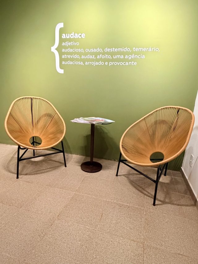 Recepção da Audace: duas poltronas de fibra natural diante da parede verde com o verbete de “audace” pintado em branco