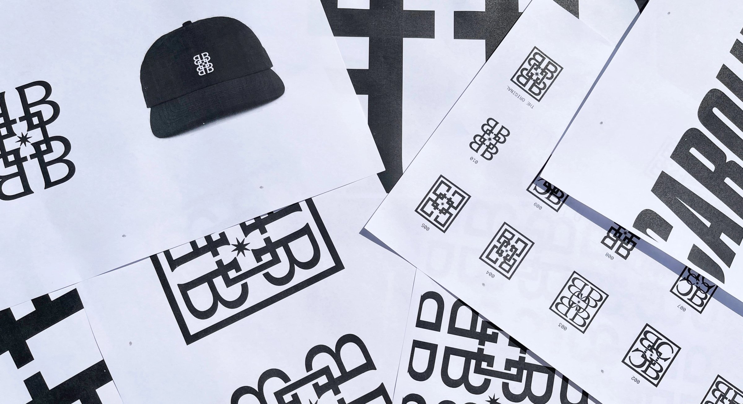 Monogram sketches and a black monogram cap scattered on paper