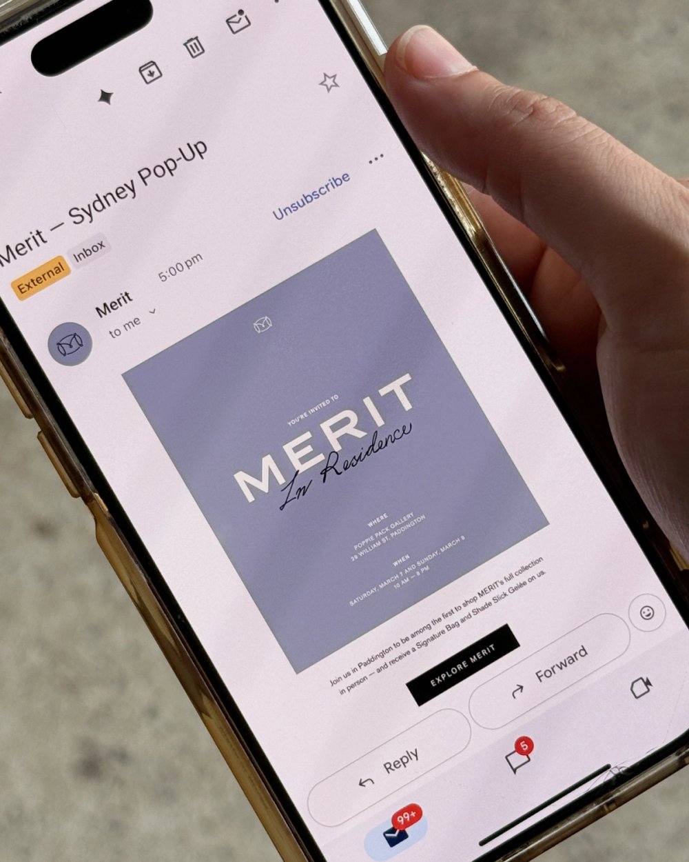 A hand holding a phone showing the MERIT Sydney pop-up email