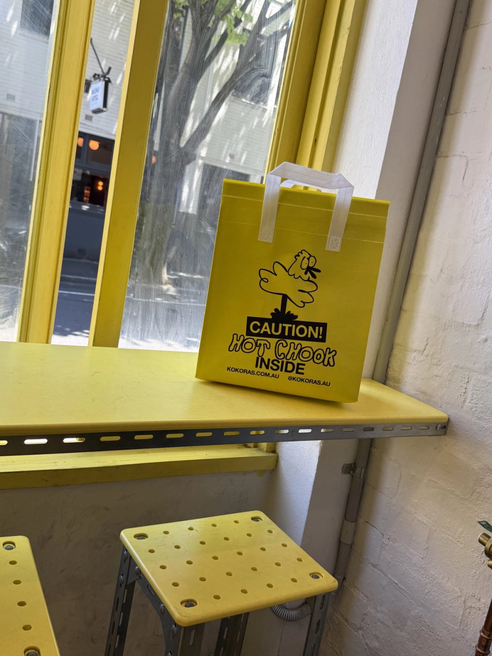 Kokoras caution bag on the window ledge above yellow stools