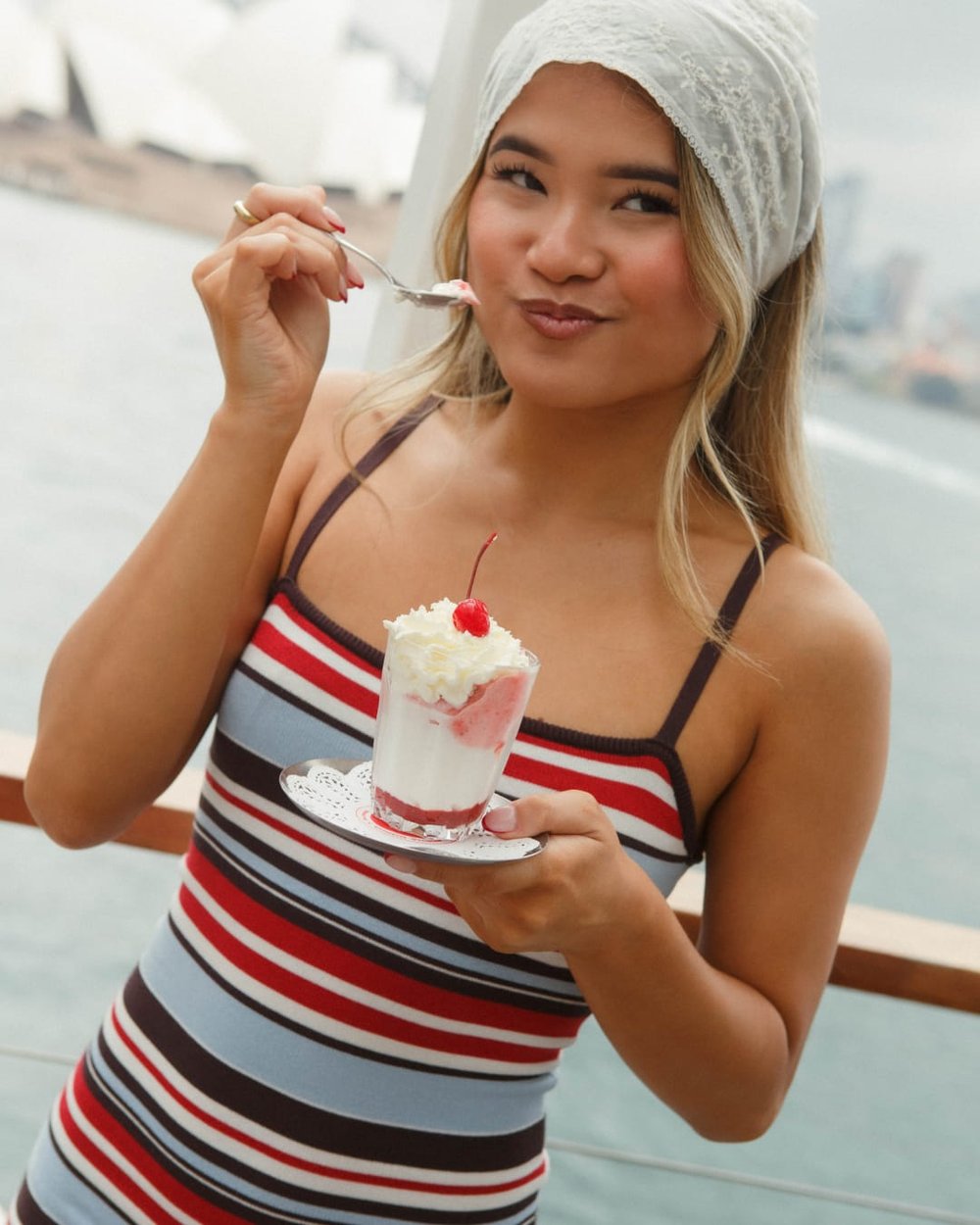 A guest in the striped Sopha Dopha x Supré dress eating a sundae on Sydney Harbour