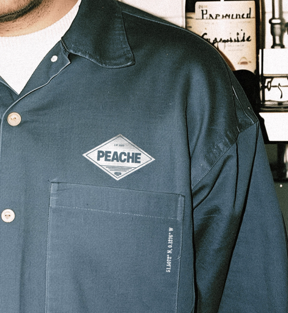 Green work shirt with a Peache diamond badge on the chest