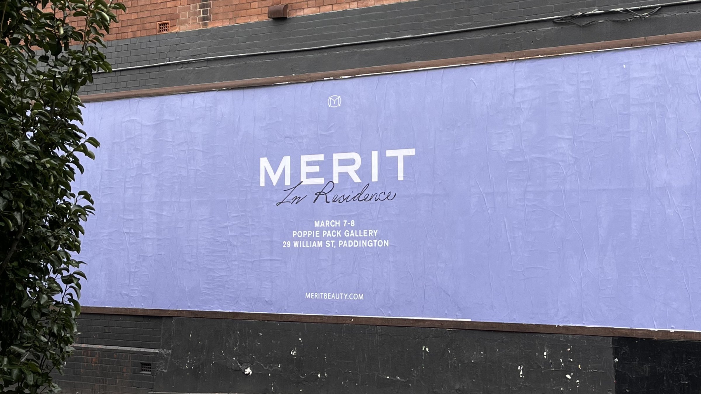 The lilac MERIT In Residence poster pasted across a street wall in Sydney