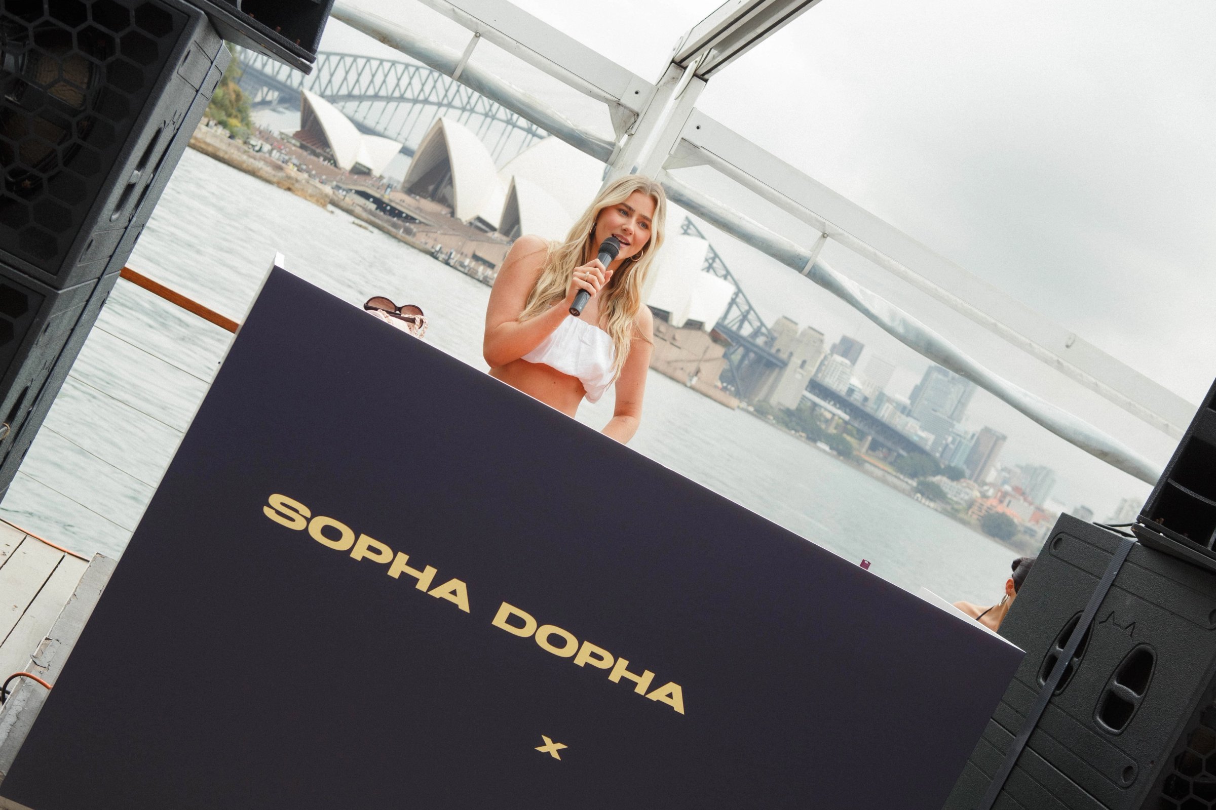 Soph on the mic behind the Sopha Dopha x Supré DJ booth, the Opera House and Harbour Bridge behind