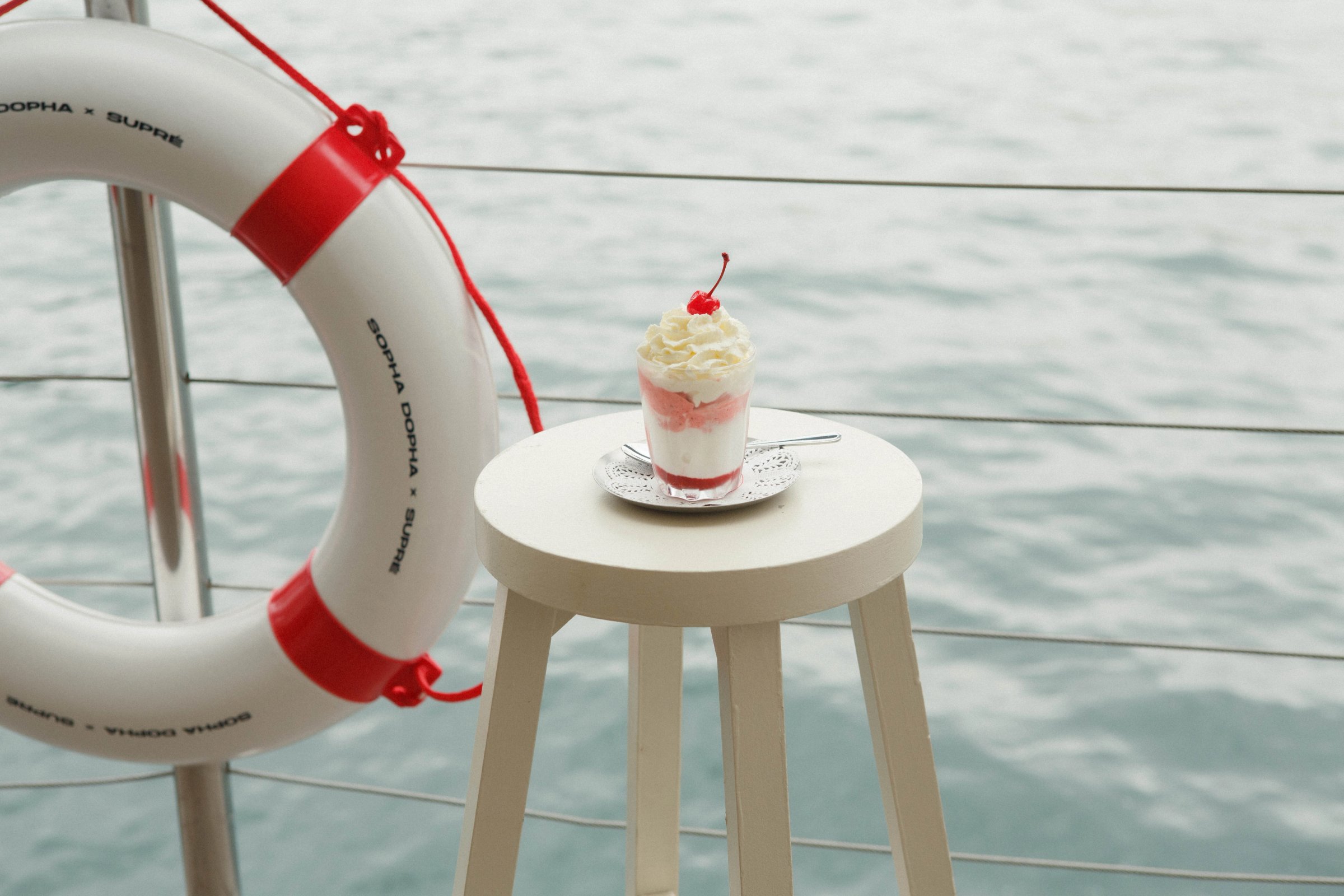 A sundae on a stool by the water, a Sopha Dopha x Supré life ring beside it