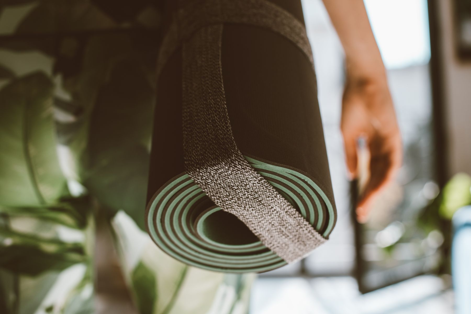 A person holding a rolled exercise mat.