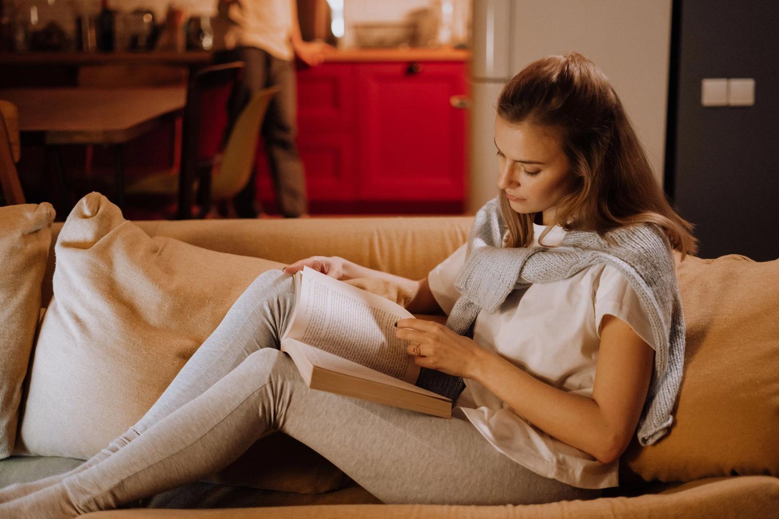 A woman reading a book while resting on a sofa.