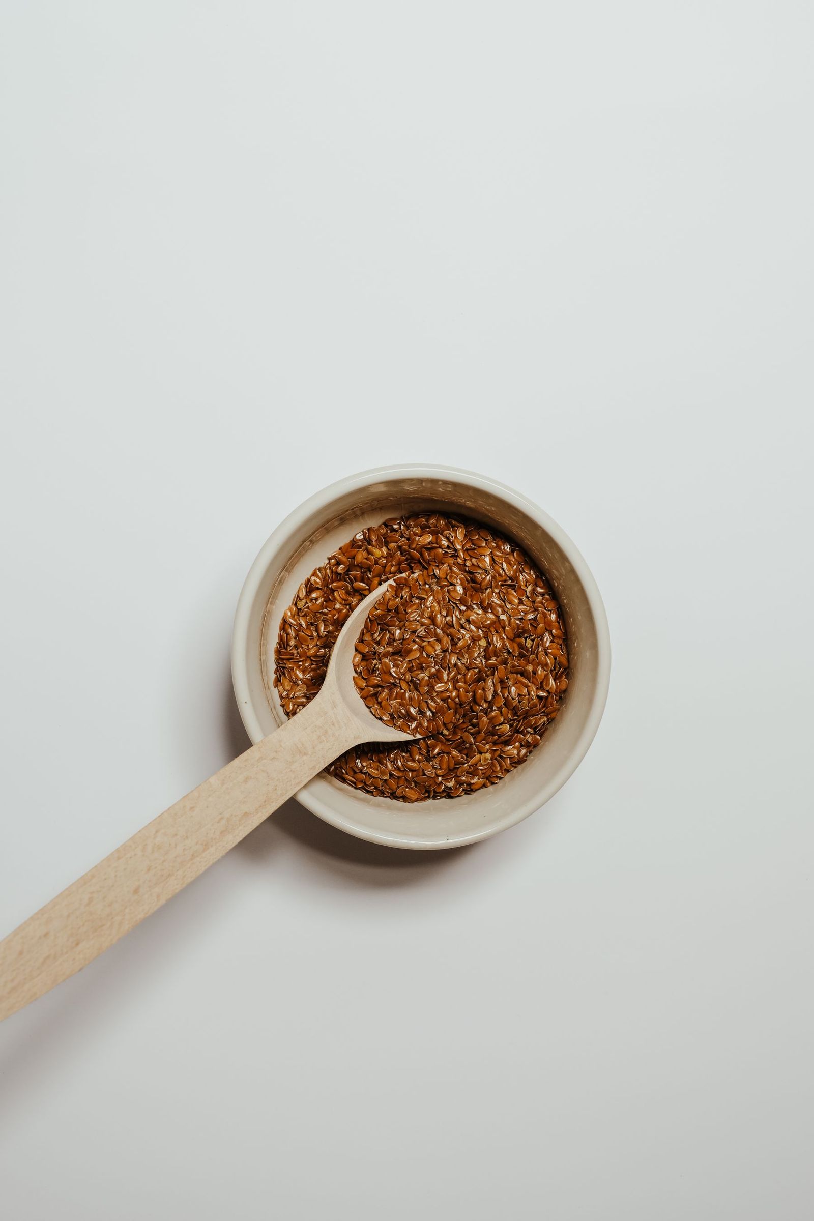 Flax seeds in a bowl with a wooden spoon.