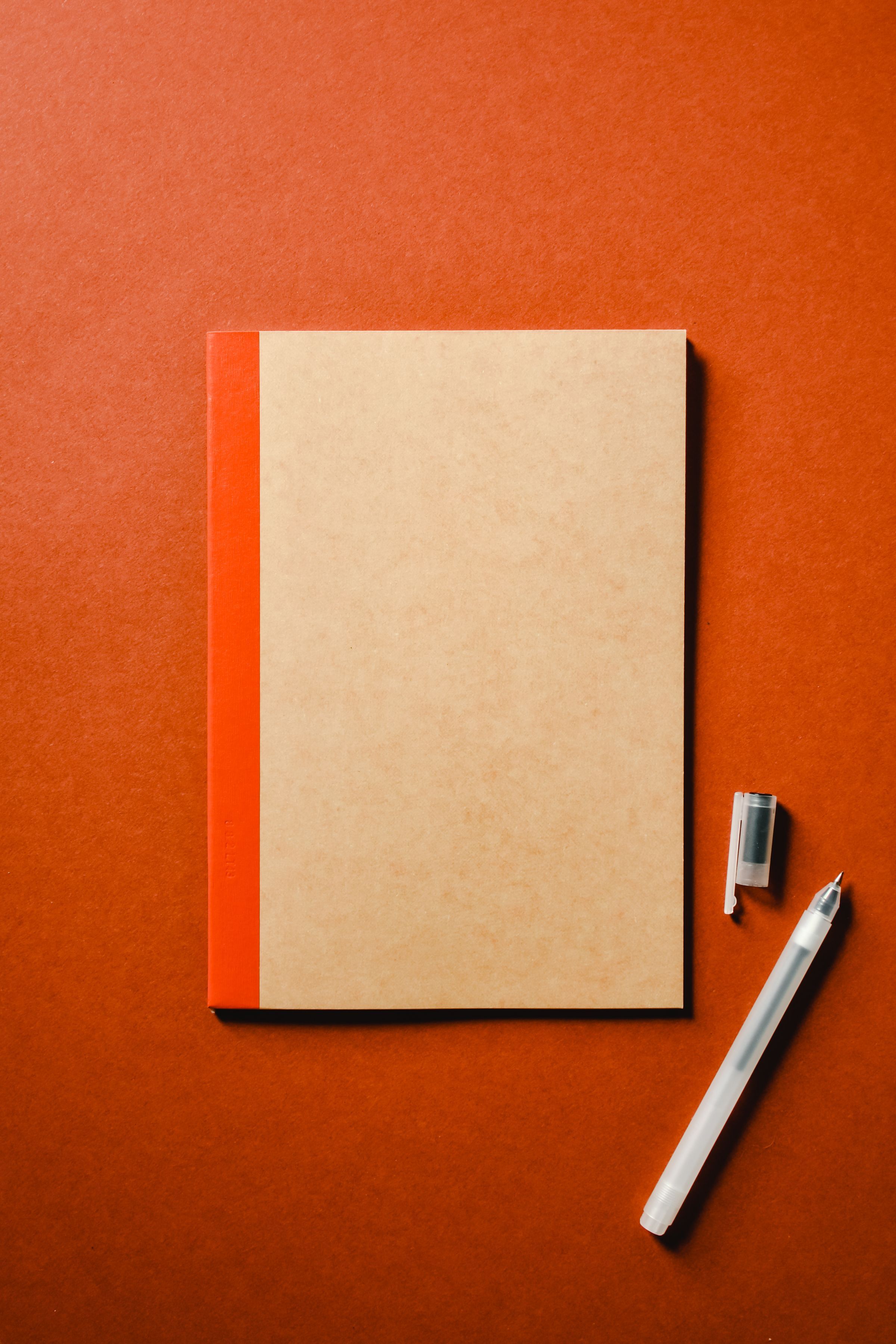 A closed notebook and pen on an orange surface.