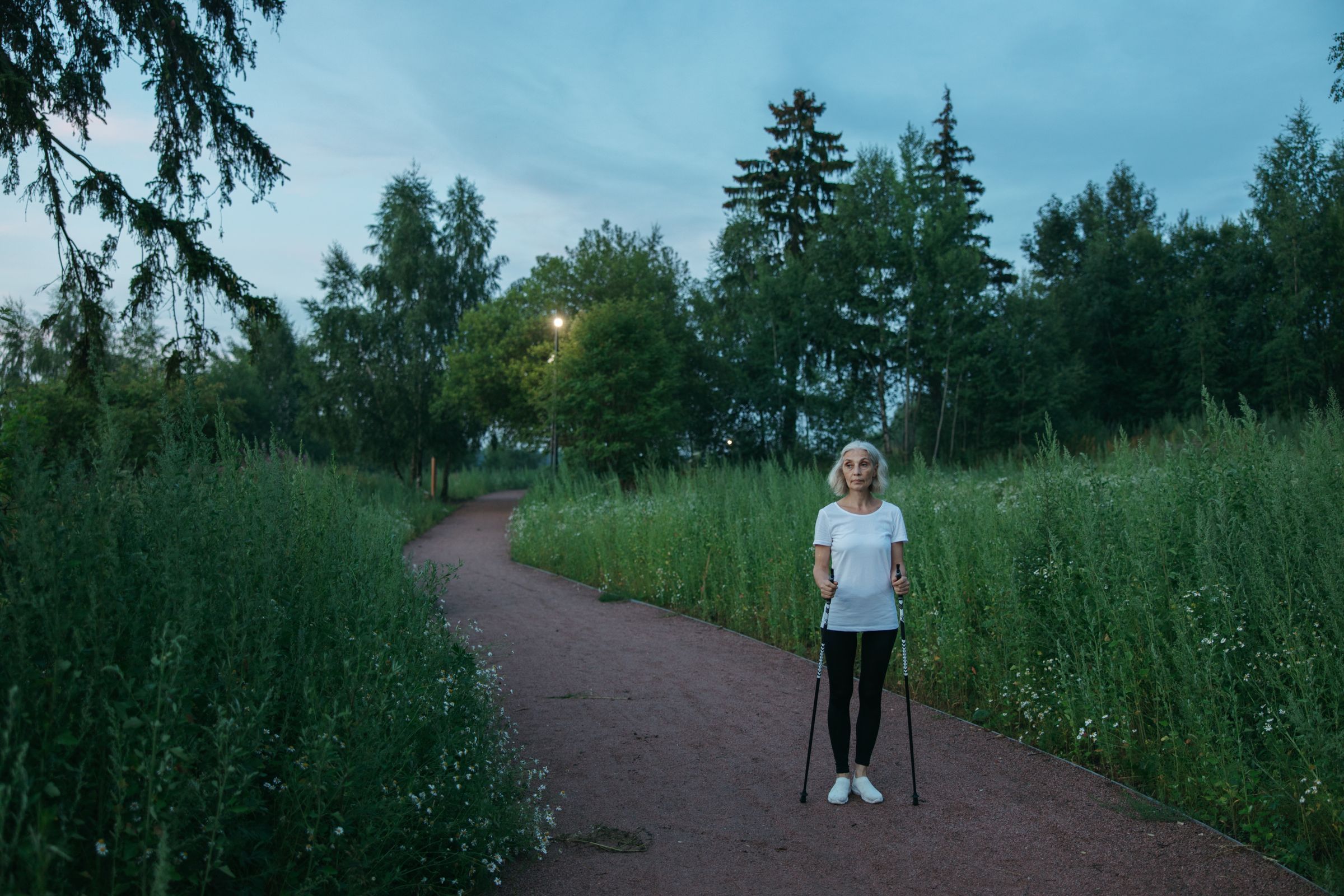 A woman walking with poles along a tree-lined path.