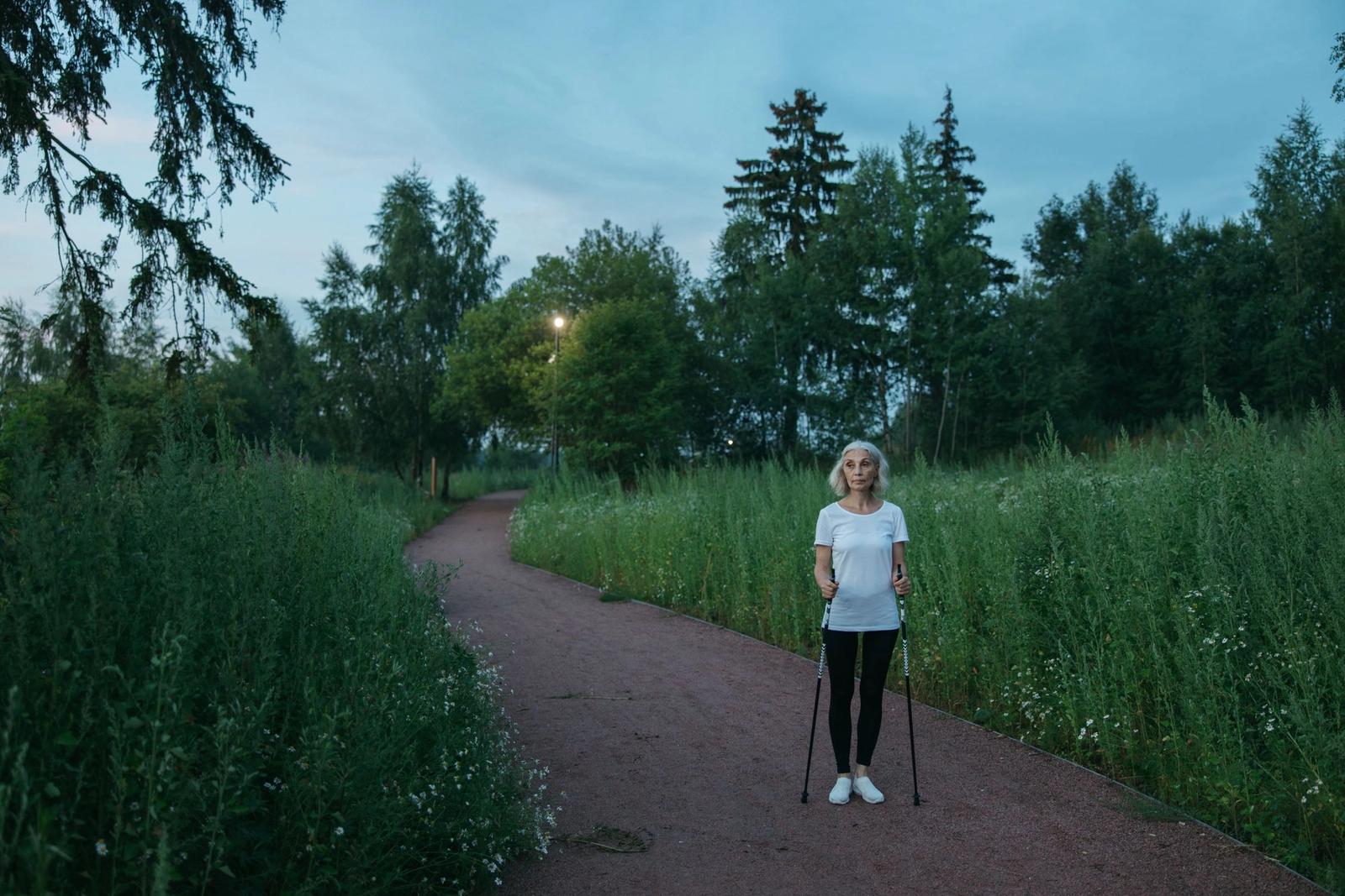 A woman walking with poles along a tree-lined path.